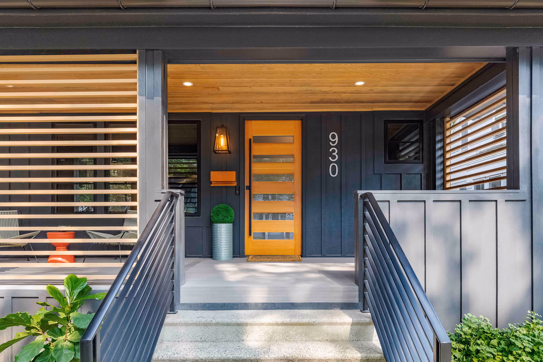 Modern bungalow exterior with charcoal siding, a wood slat screen wall, and a wood front door with house numbers
