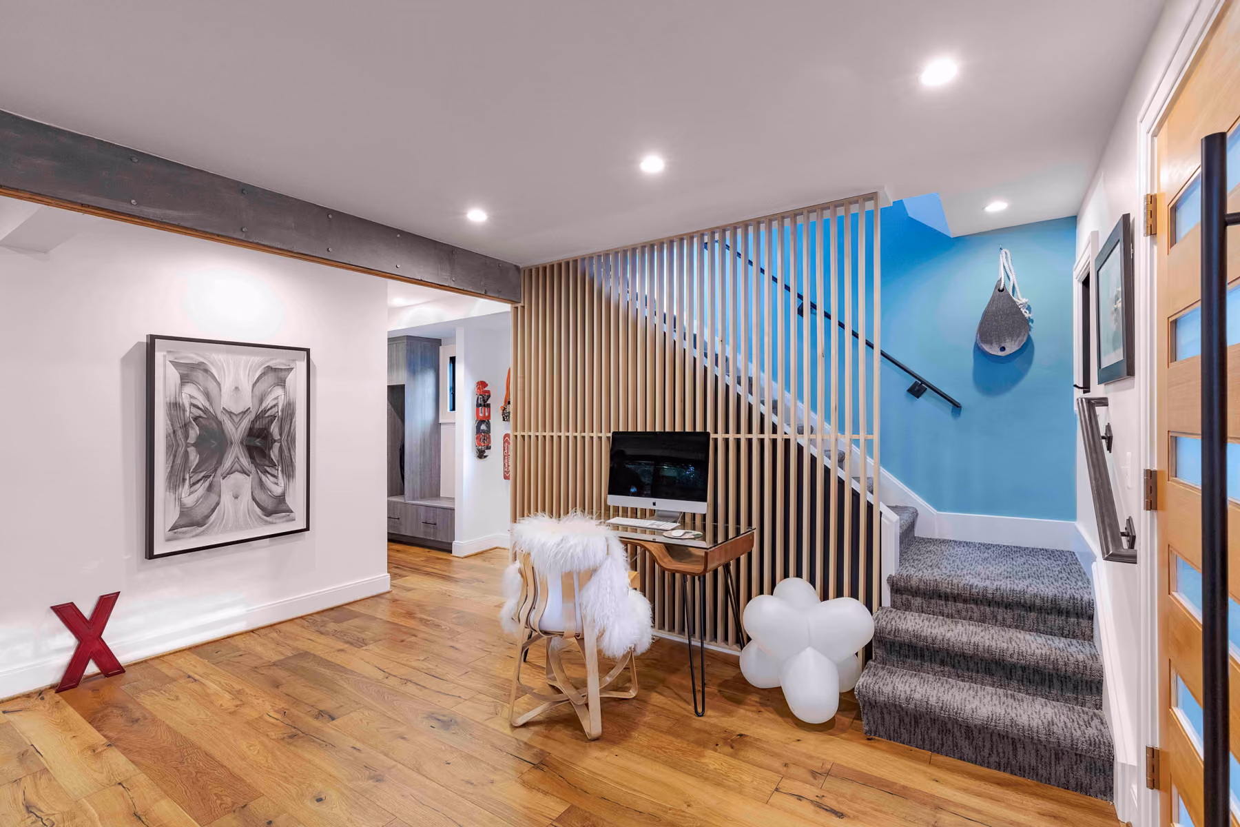 Open-plan lower level with a wood-slat staircase screen, a bright blue accent wall, and a curated art and collectibles display