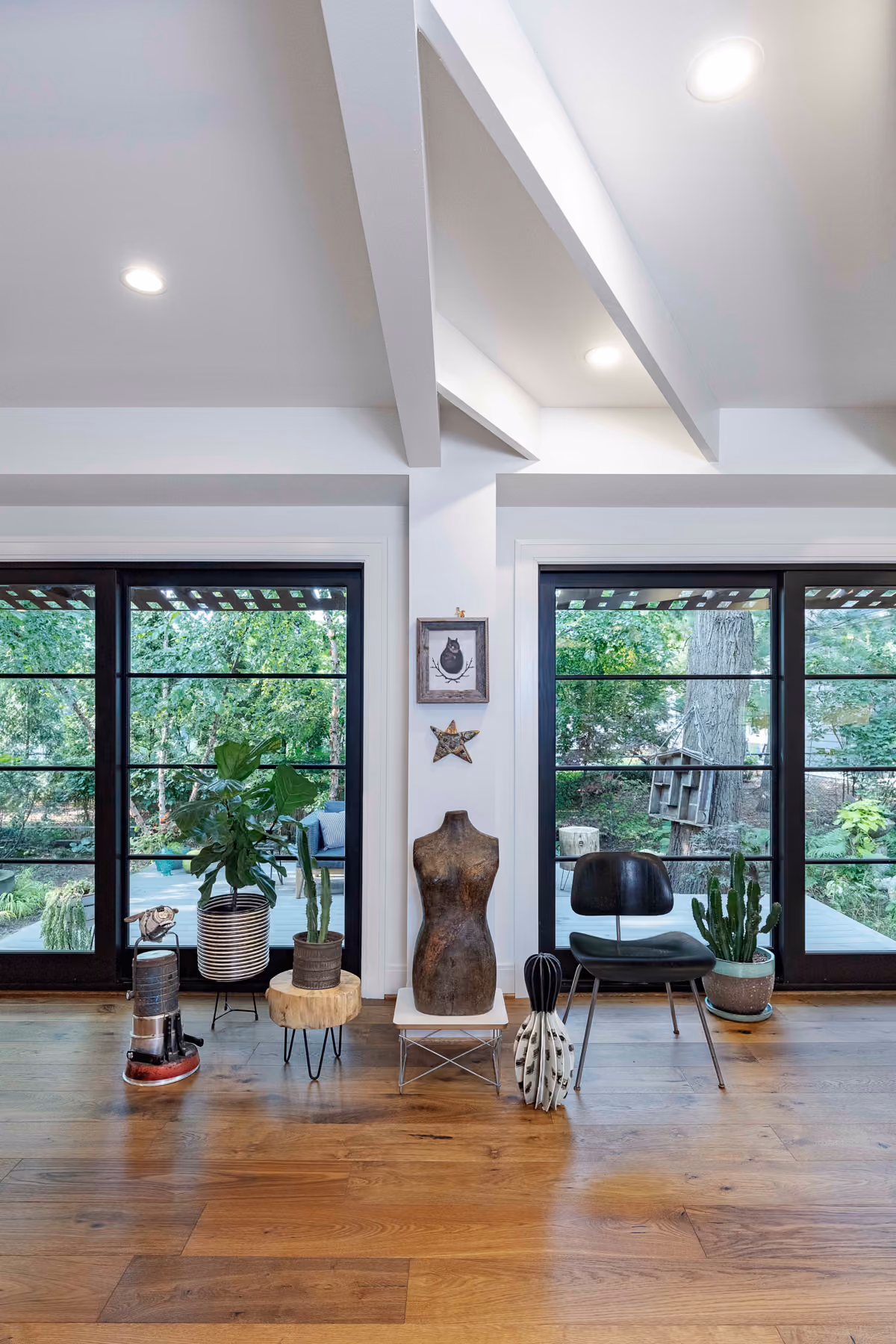 Vaulted living space with tall black-framed windows, a vintage dress form displayed as sculptural art, and houseplants