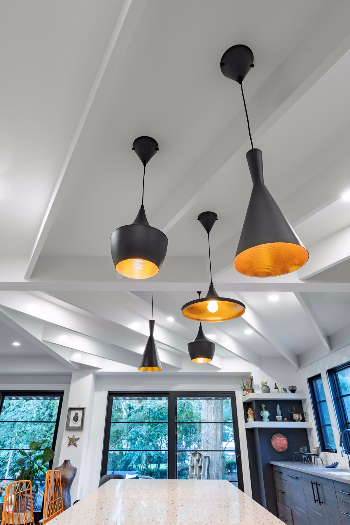 Kitchen island with a cluster of black and gold cone pendant lights under a vaulted beamed ceiling