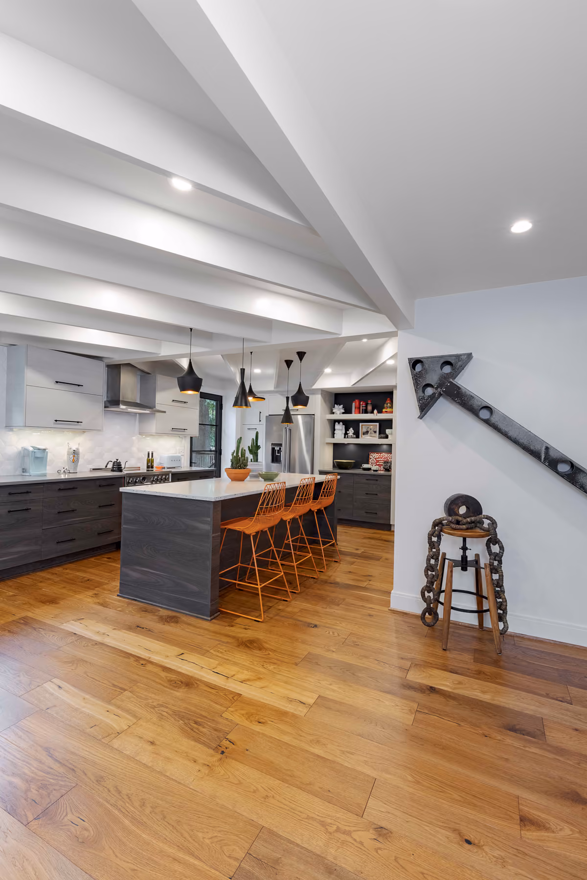 Kitchen island with orange counter stools, black pendant lights, and a wall-mounted decorative sculpture