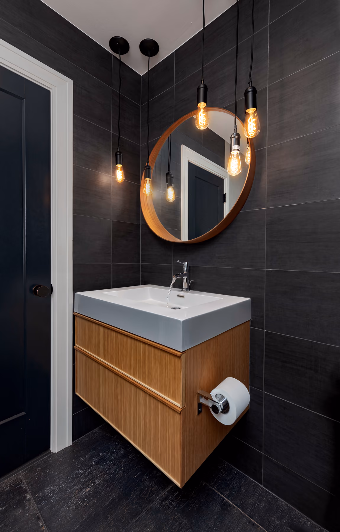 Powder room with dark stone tile walls, a floating wood vanity, and a cluster of pendant Edison bulb lights