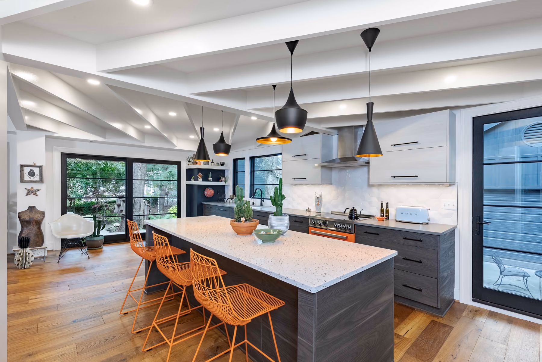Kitchen with white upper cabinets, dark lower cabinets, a terrazzo-look island, and orange counter stools under a vaulted beamed ceiling