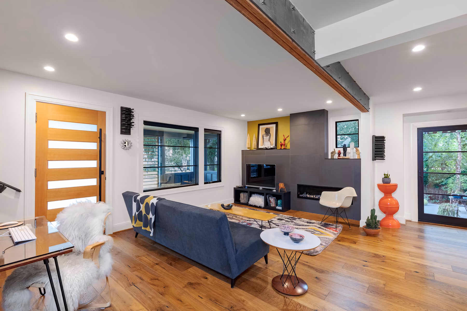 Living room with a modern gray fireplace surround, navy sofa, mid-century chair, and glass front door