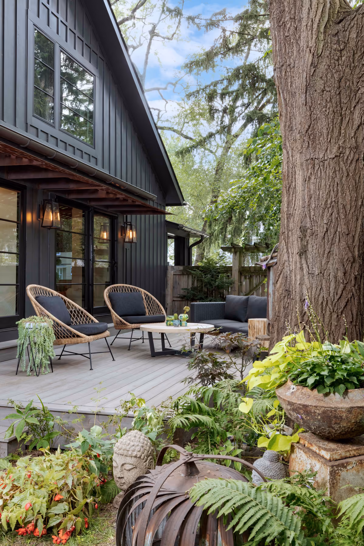 Backyard patio with dark board-and-batten siding, a wood pergola, and lush garden landscaping