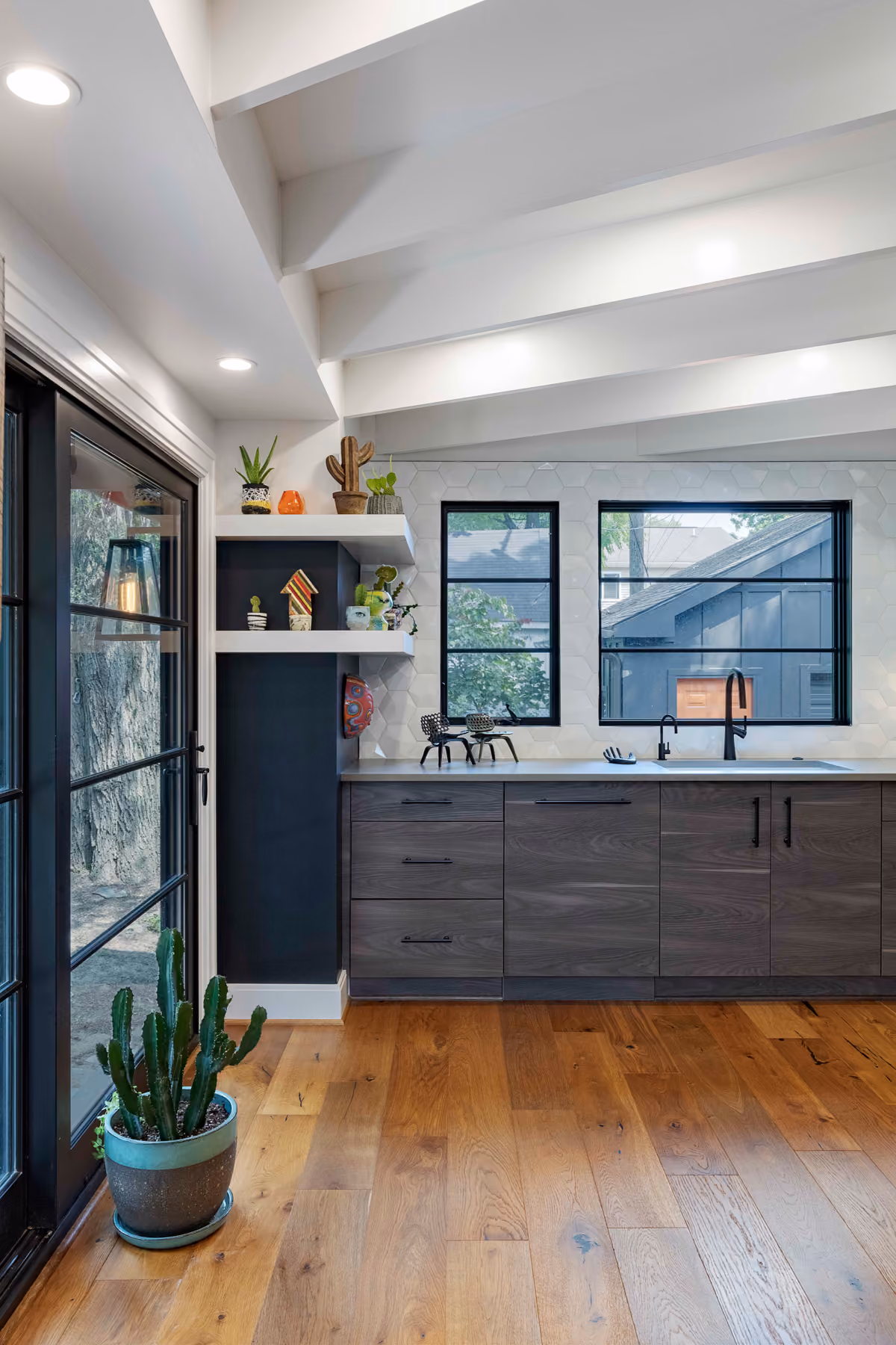 Kitchen sink area with dark wood-tone cabinetry, a vaulted white beamed ceiling, and black-framed windows