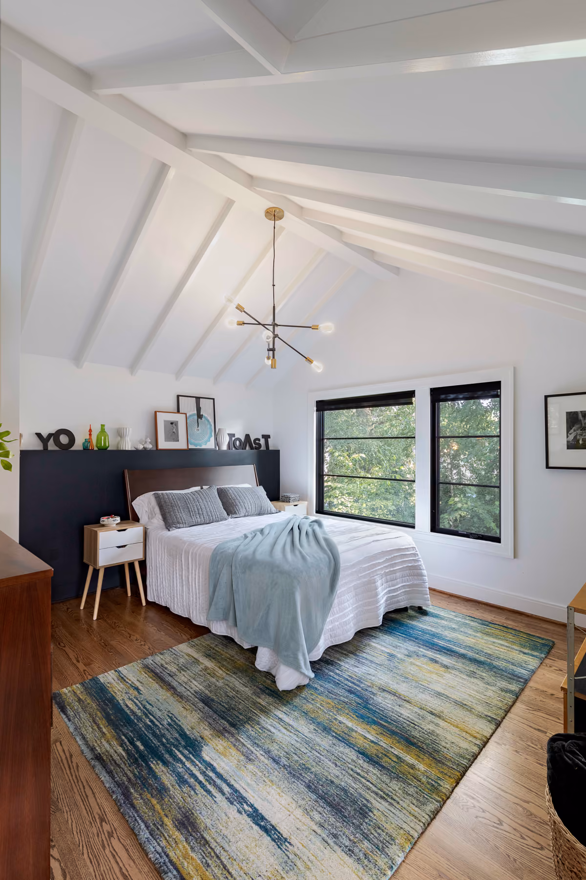 Bedroom with a vaulted ceiling, brass chandelier, black upholstered headboard, and a blue and green area rug
