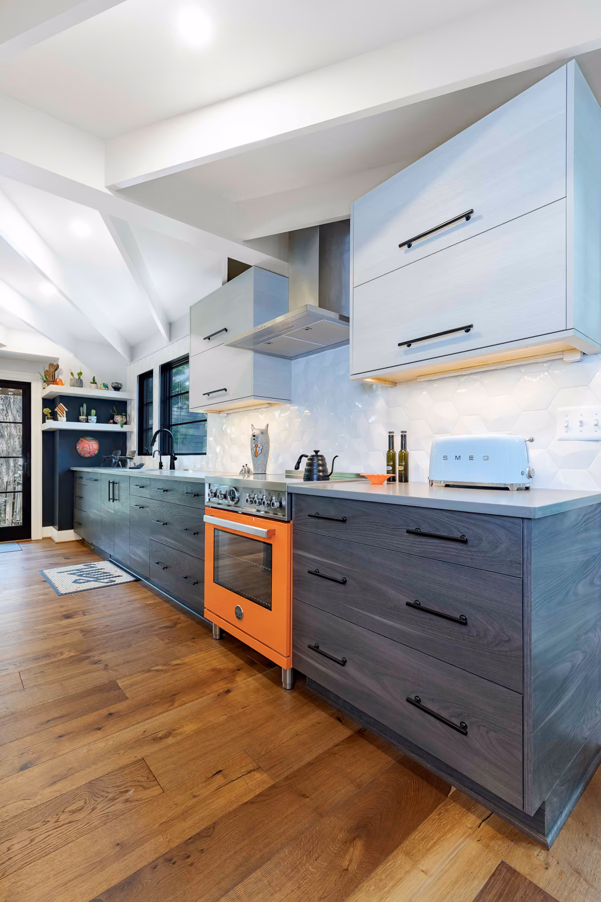 Kitchen range wall with a bold orange oven range, white upper cabinets, and dark wood-tone lower cabinets