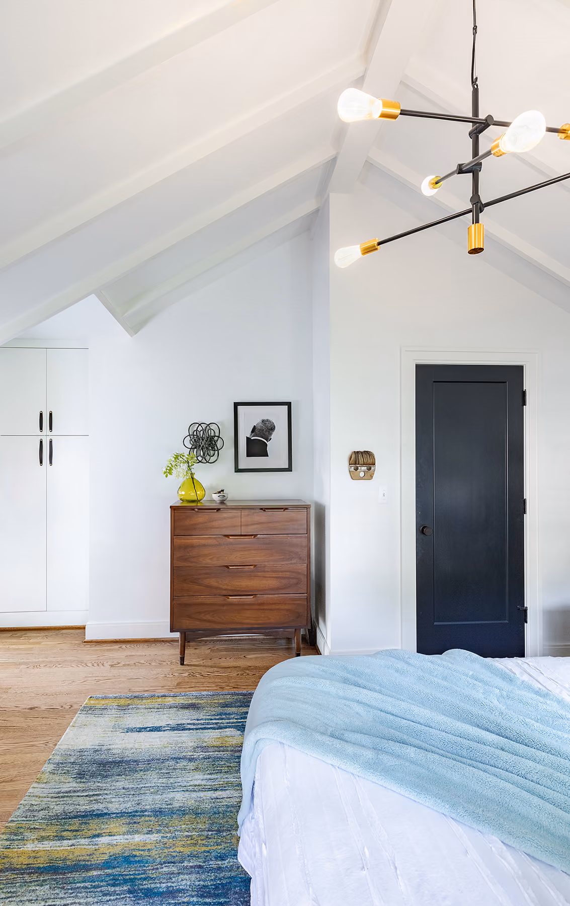 Bedroom with a vaulted ceiling, sculptural brass chandelier, and a walnut dresser
