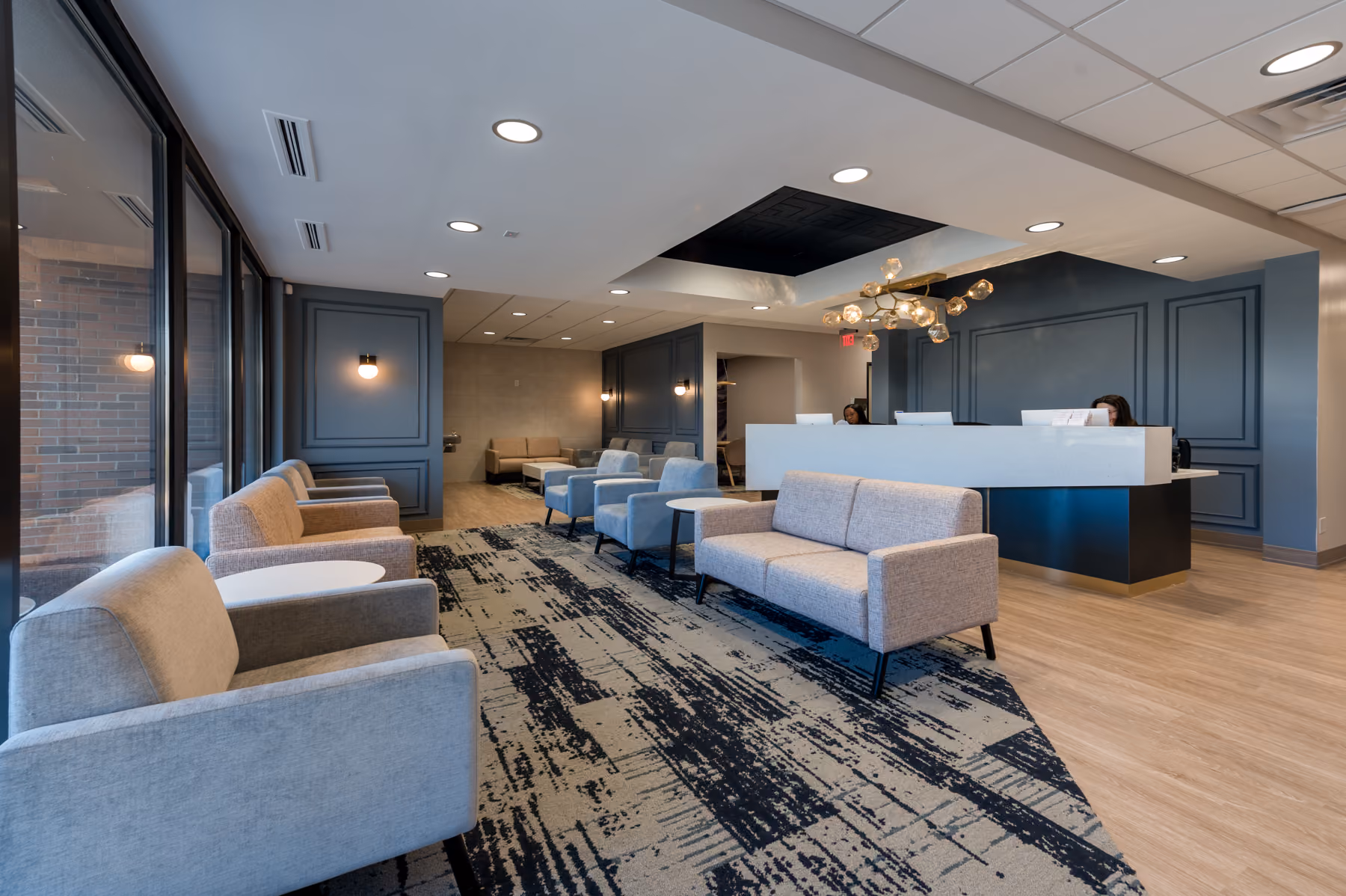 Reception lobby of a medical office with navy paneled walls, gray lounge seating, and a brass sputnik pendant light