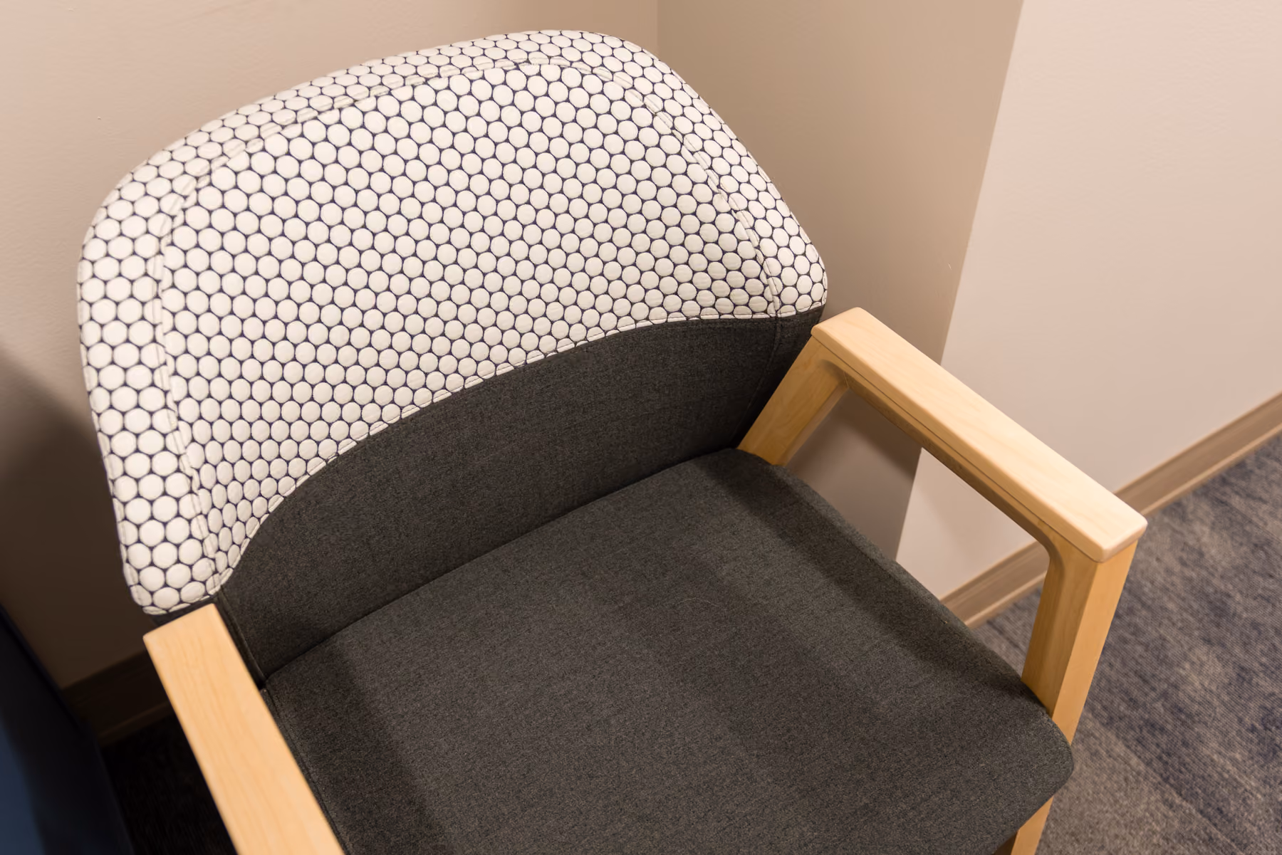Detail of a wood-framed chair with a charcoal seat and dot-print upholstered back