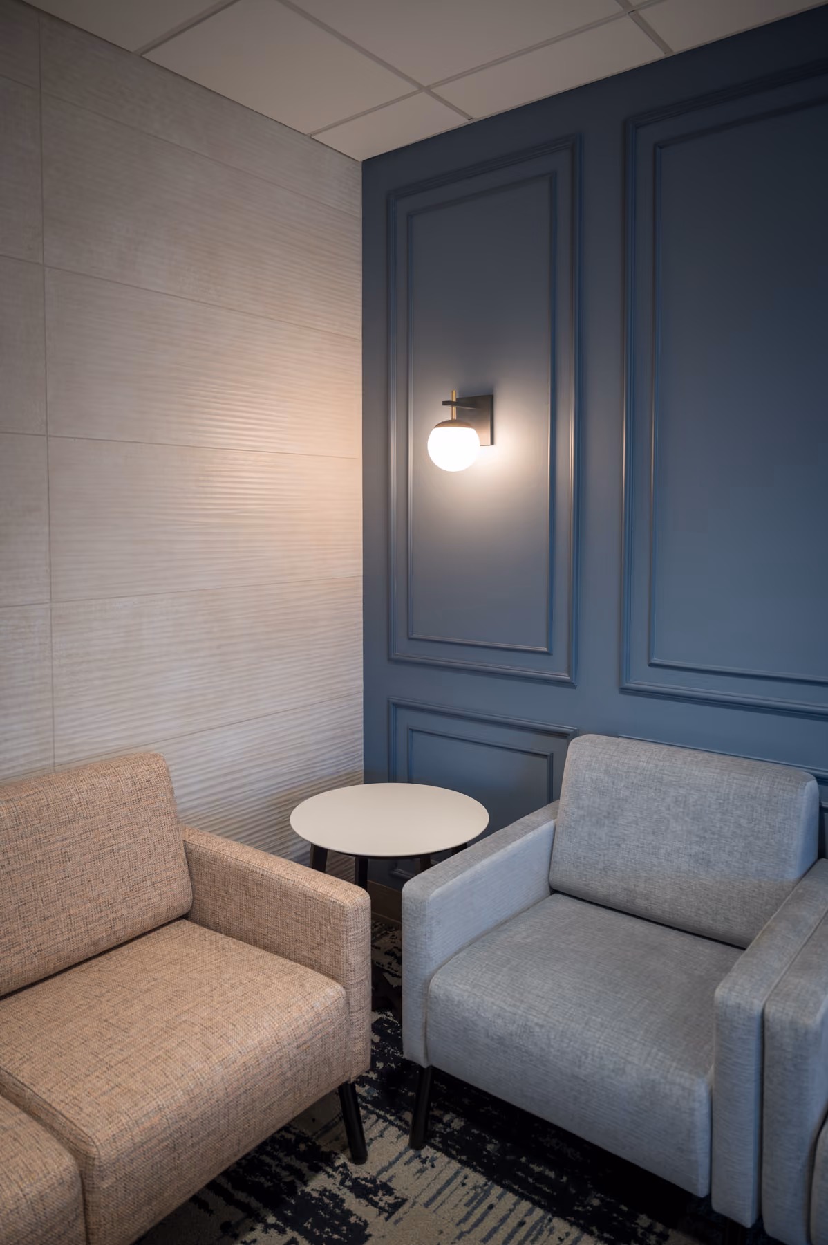 Waiting room corner with textured wall paneling, a navy accent wall, and tan and gray lounge chairs