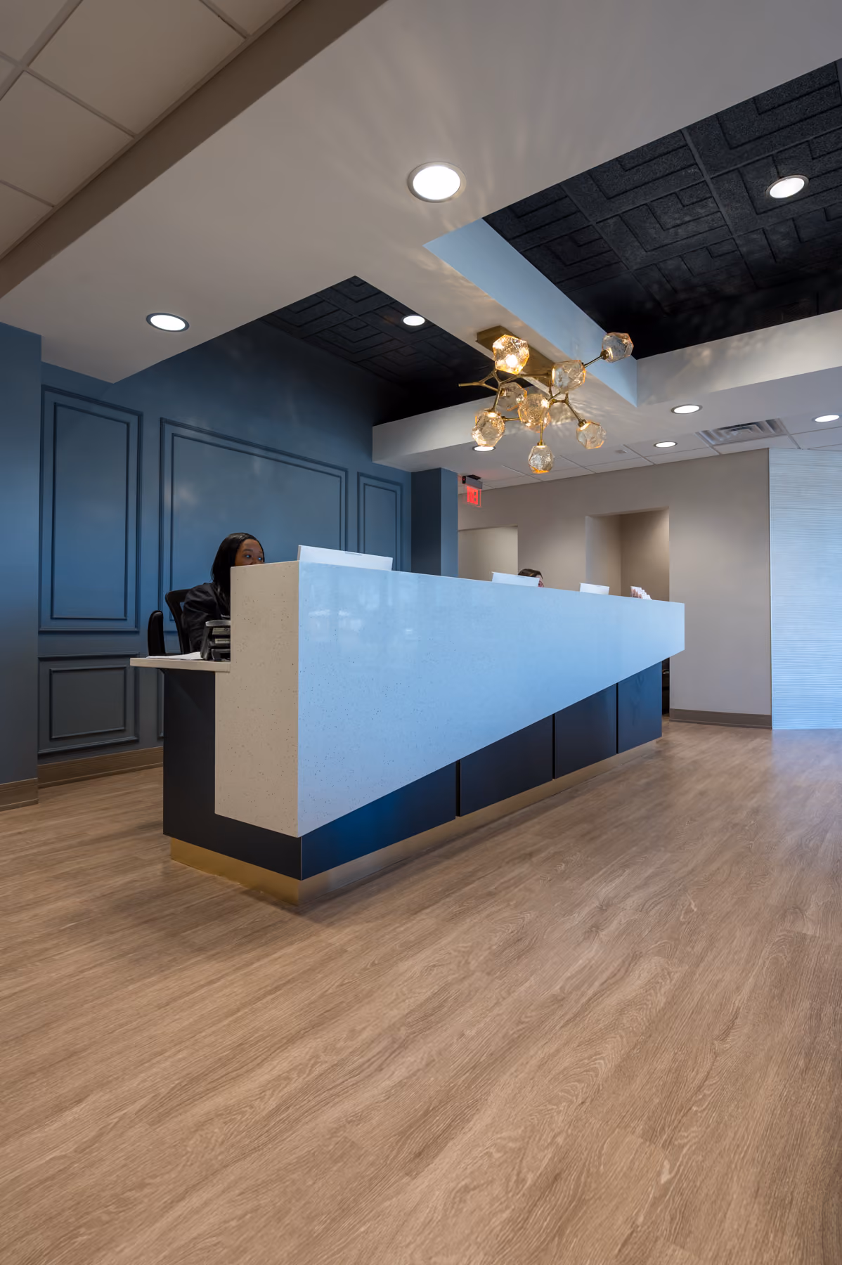 Reception desk with a black tray ceiling detail, navy paneled wall, and a brass sputnik pendant light