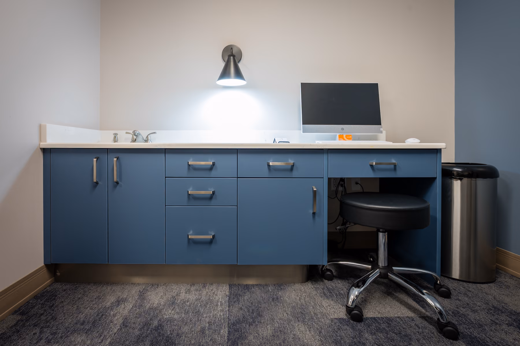 Exam room with blue built-in cabinetry, an integrated sink, and a rolling stool