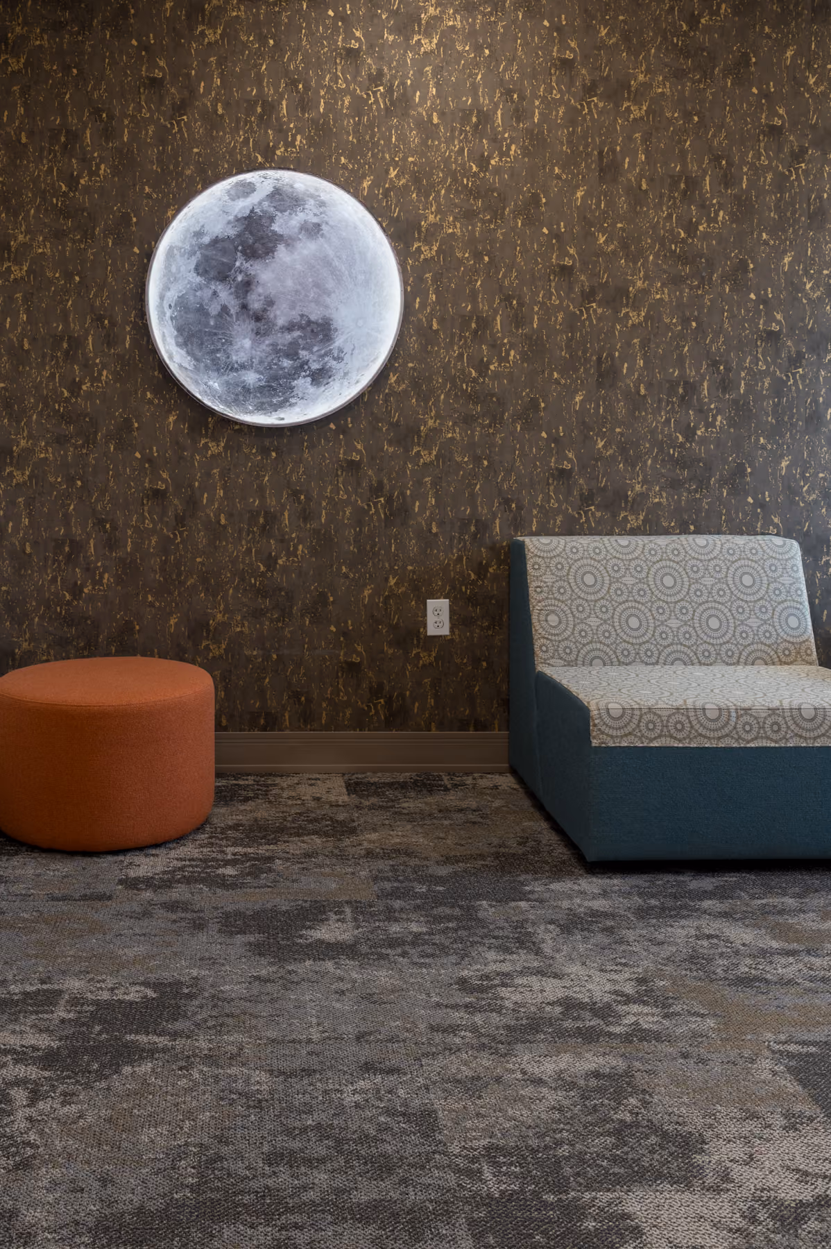 Waiting nook with moon wall art, a geometric-print teal lounge chair, and a rust-orange ottoman