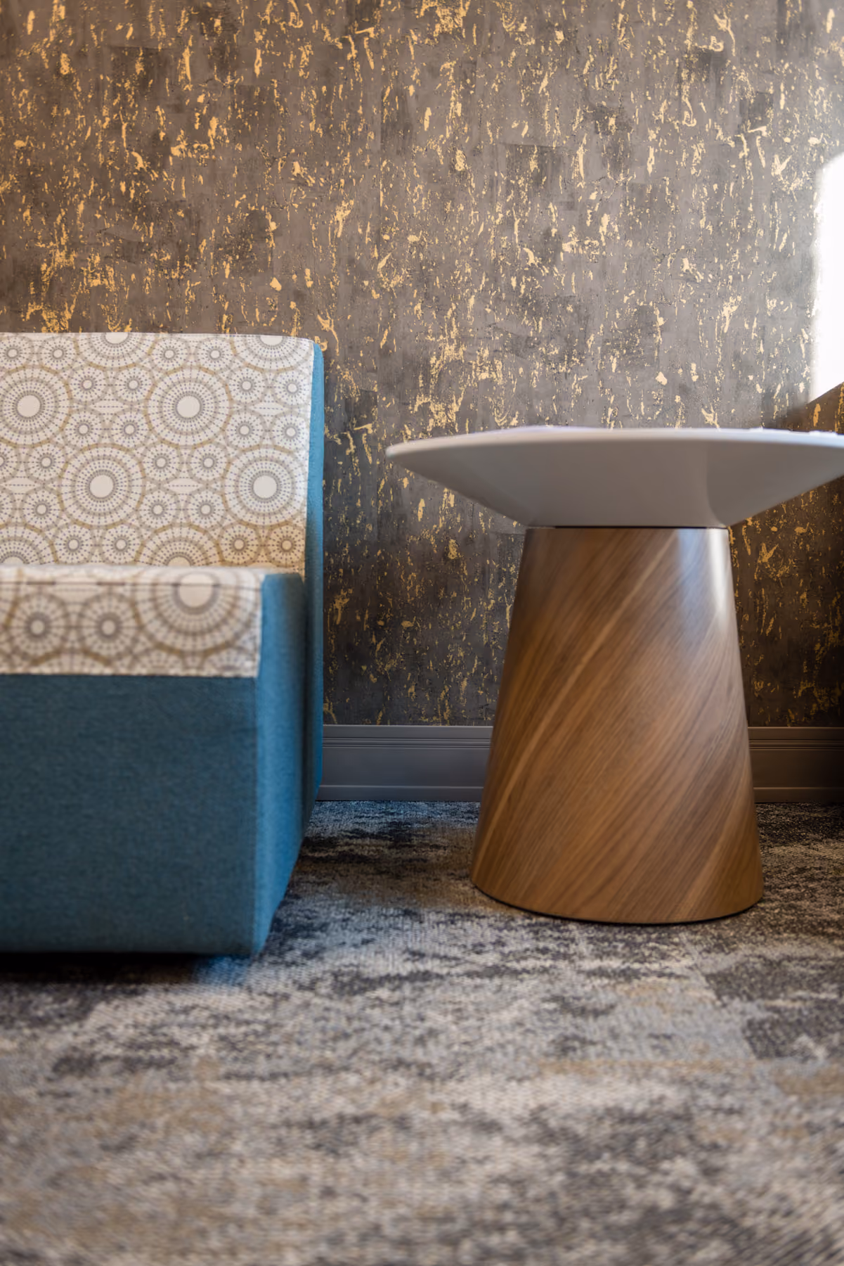 Detail of a teal geometric-print lounge chair beside a wood cone-base side table