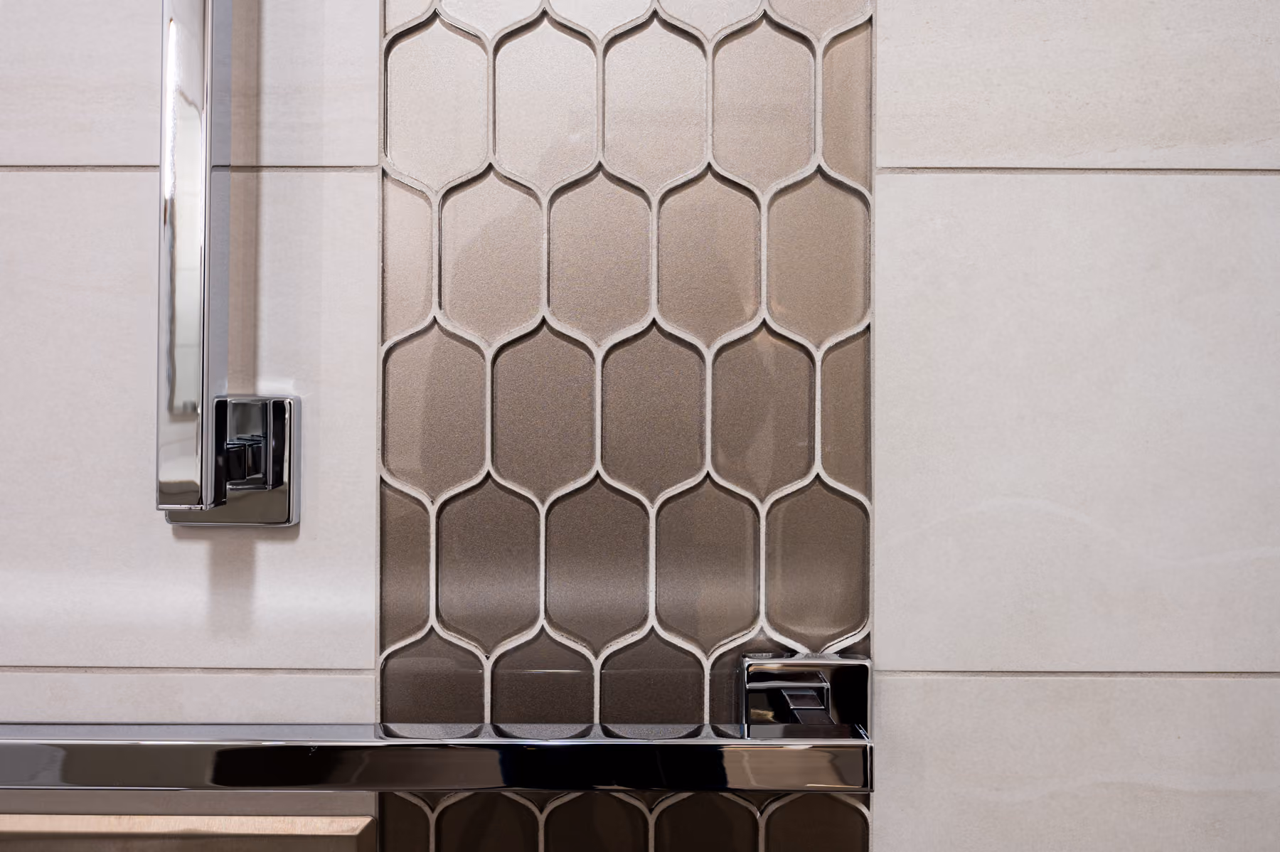 Close-up of a metallic hexagonal mosaic tile accent with a chrome grab bar