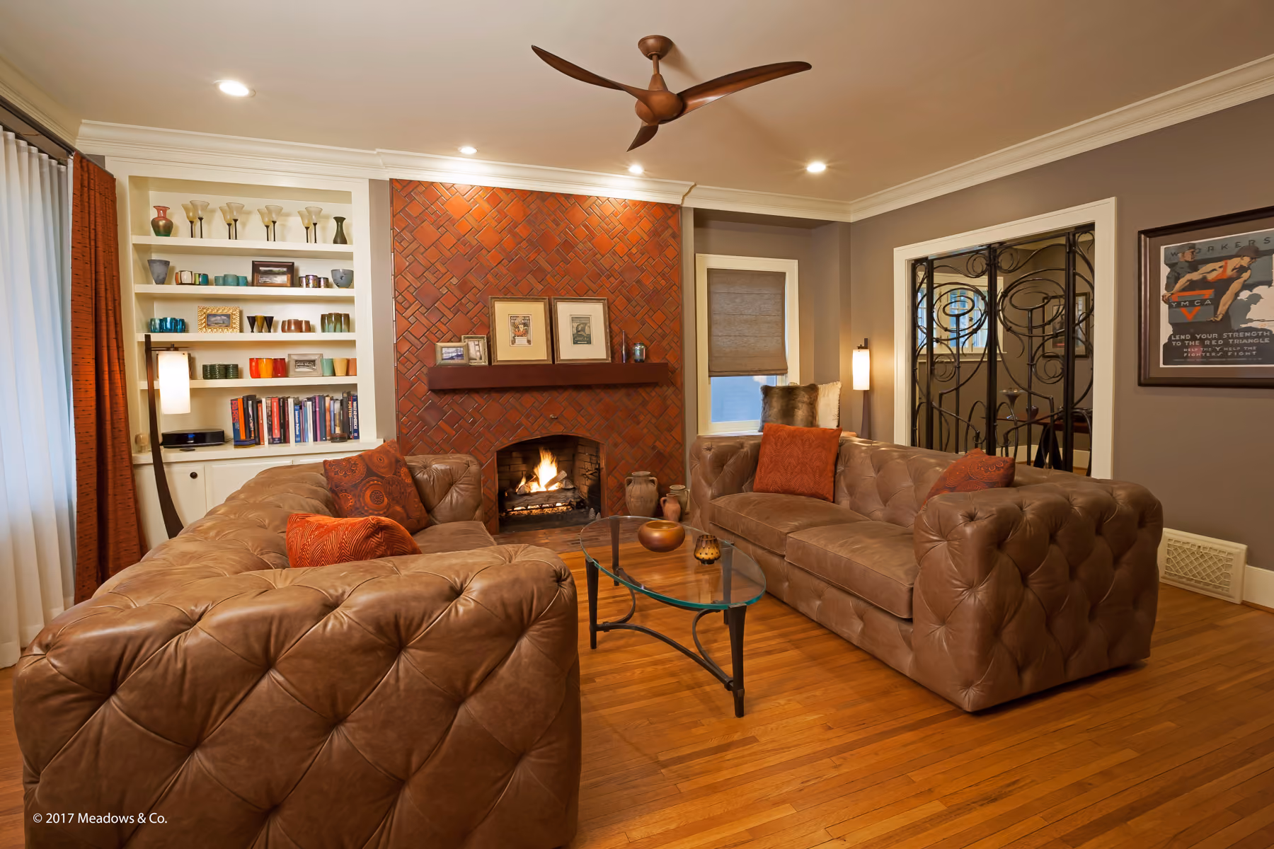 Living room with a red herringbone brick fireplace, tufted leather sectional sofas, and a custom wrought-iron interior gate