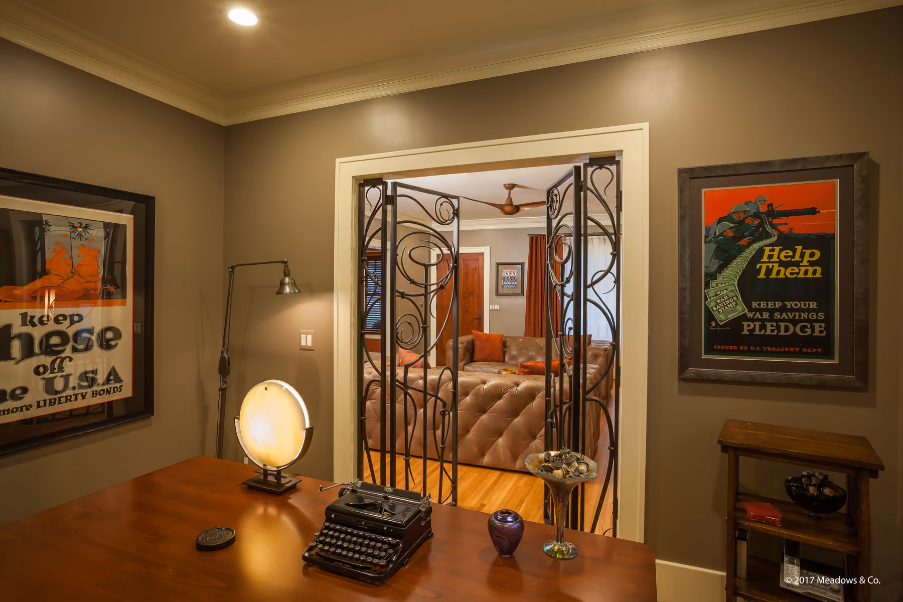 Home office with a vintage typewriter, framed vintage posters, and a view through the custom iron gate into the living room