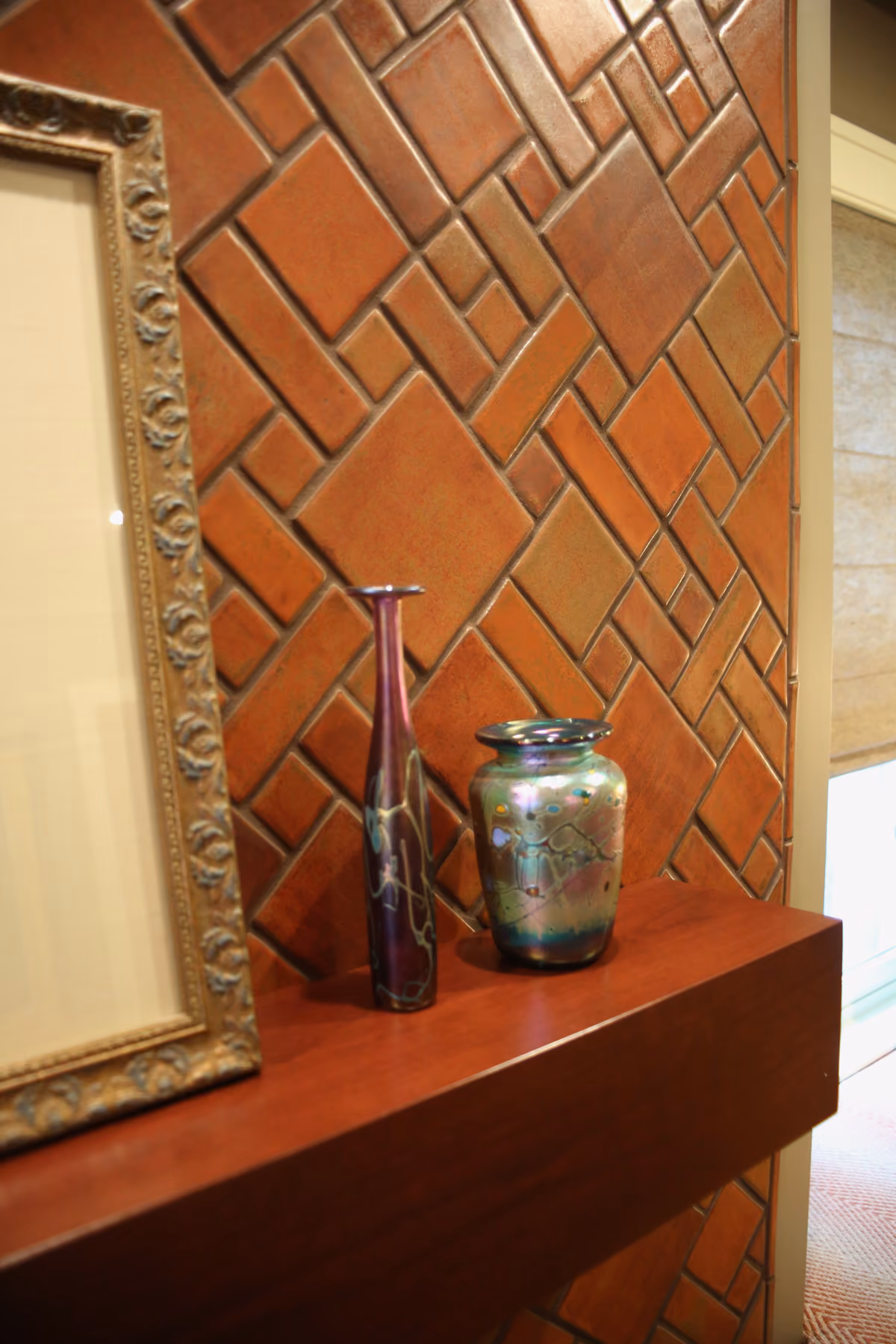 Fireplace mantel detail with a geometric brick tile pattern and art glass vases