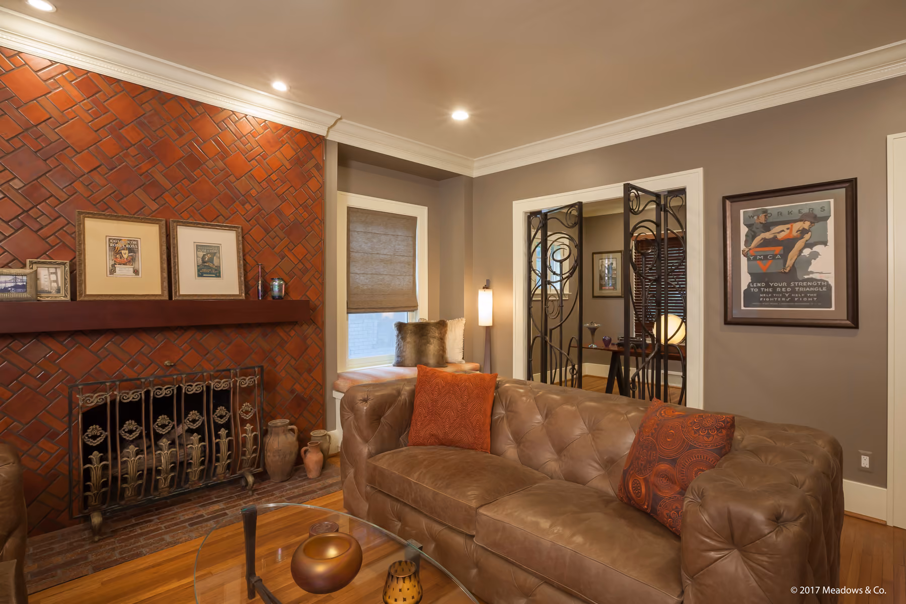 Close view of a herringbone brick fireplace with an ornate cast-iron screen and tufted leather sofa