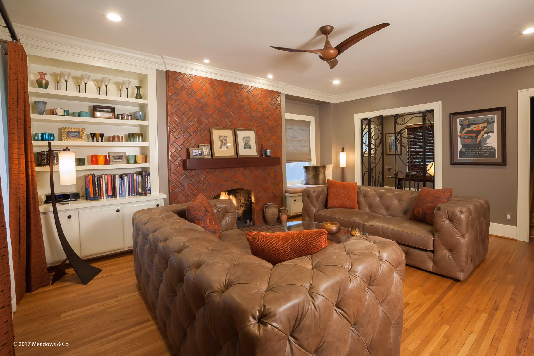 Living room with tufted leather sofas, a herringbone brick fireplace, and a custom scrollwork iron gate dividing the room
