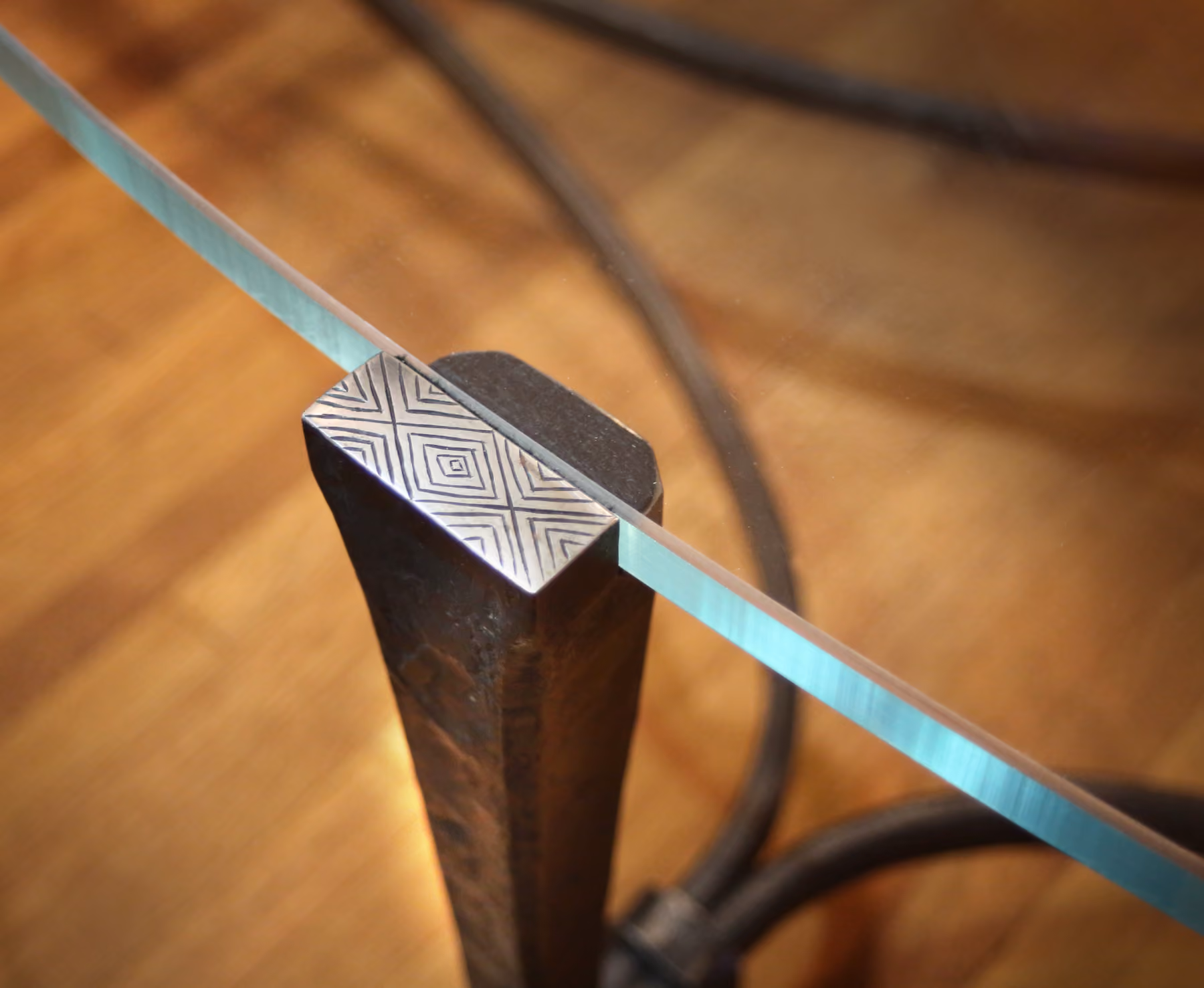 Detail of a metal coffee table leg with a diamond-etched pattern and glass tabletop