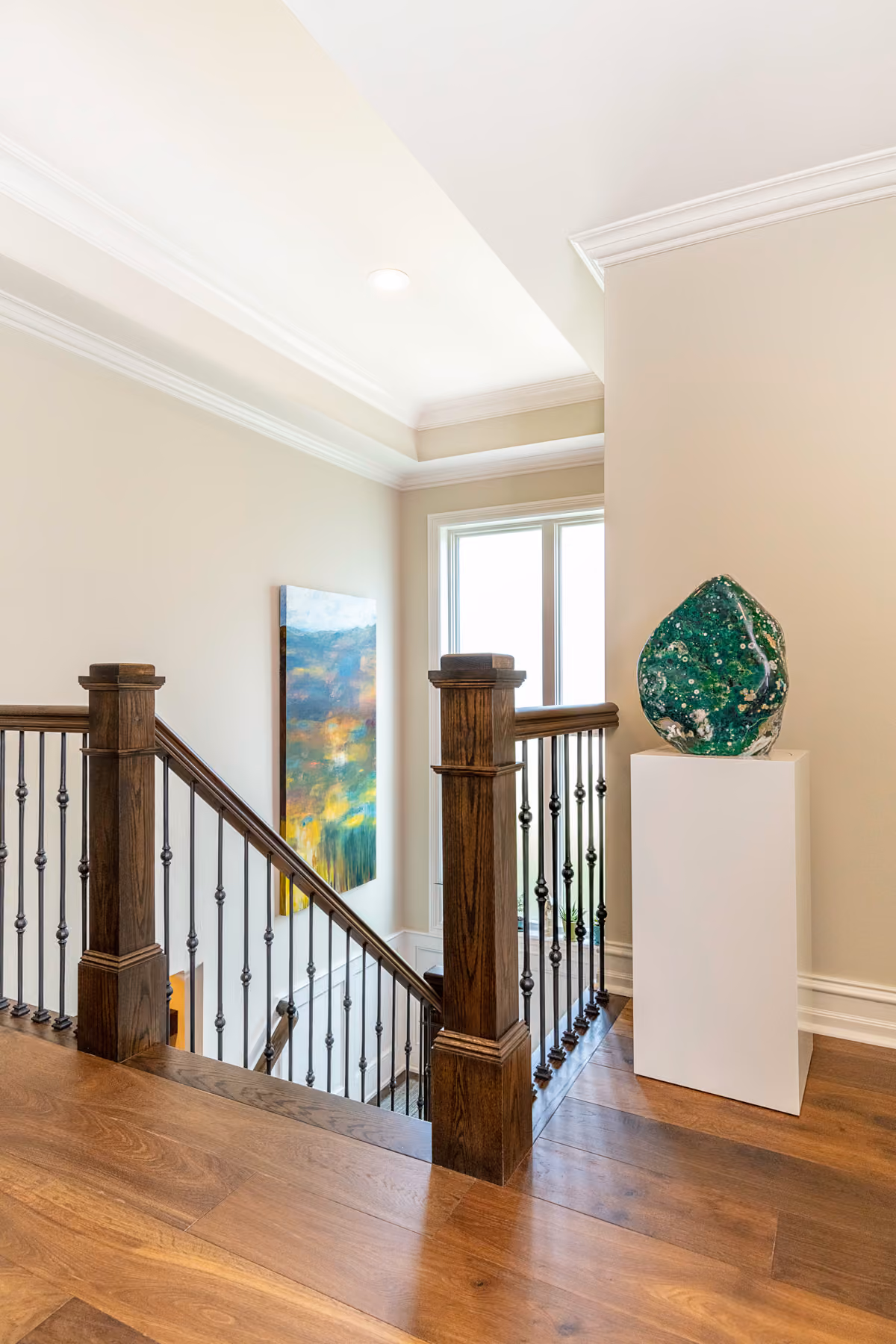 Stairway landing with dark wood newel posts, wrought-iron balusters, and a large polished stone geode sculpture on a pedestal