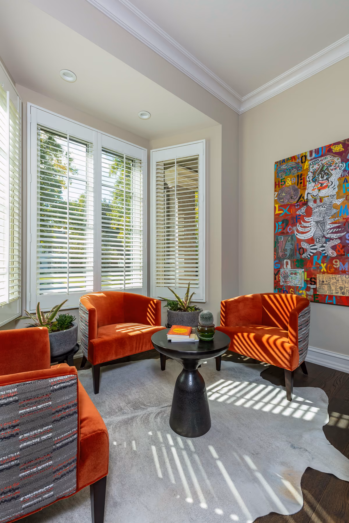 Bay window sitting nook with orange striped velvet armchairs, a black pedestal table, and a cowhide rug
