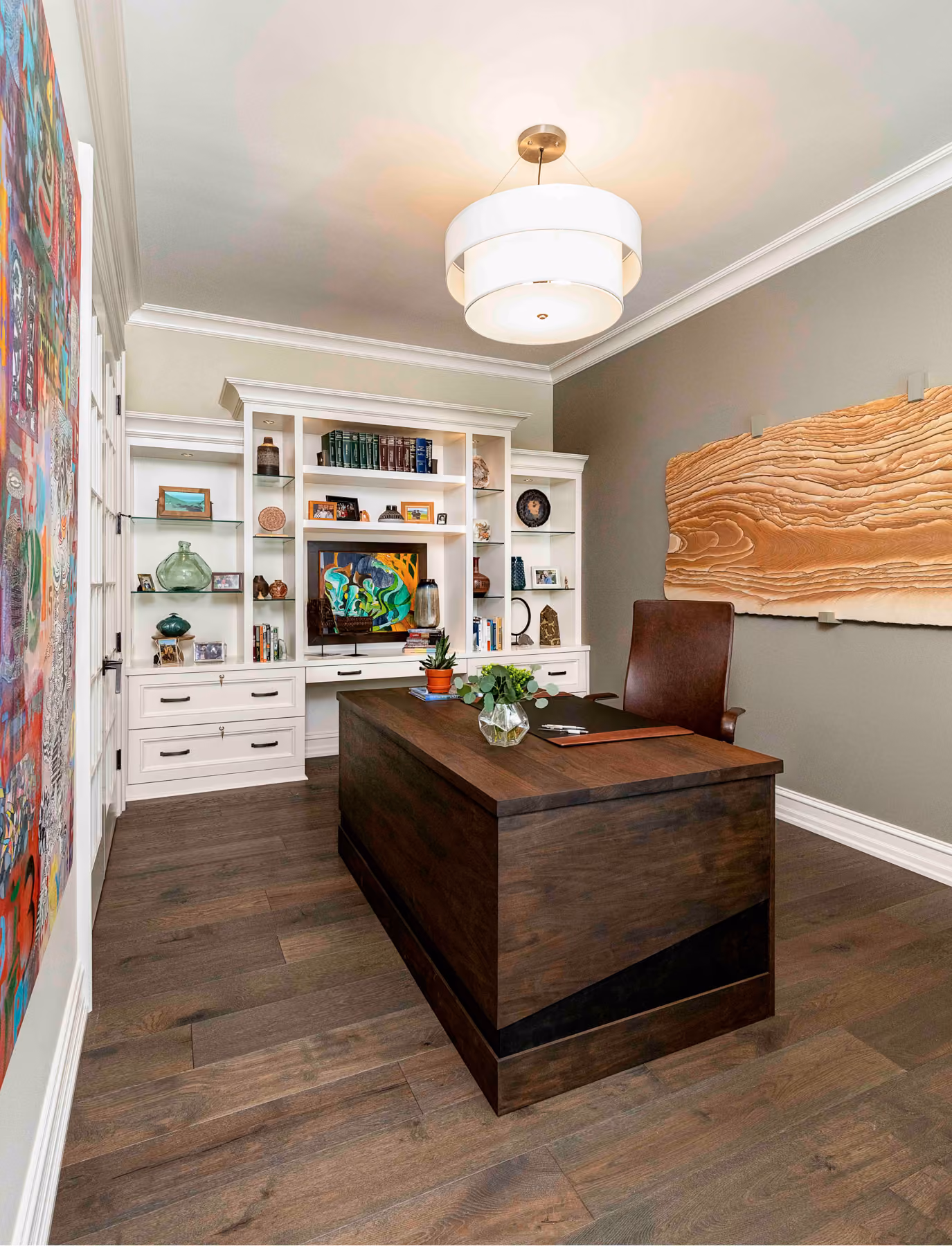 Home office with a dark wood desk, white built-in bookshelves, and a colorful abstract painting