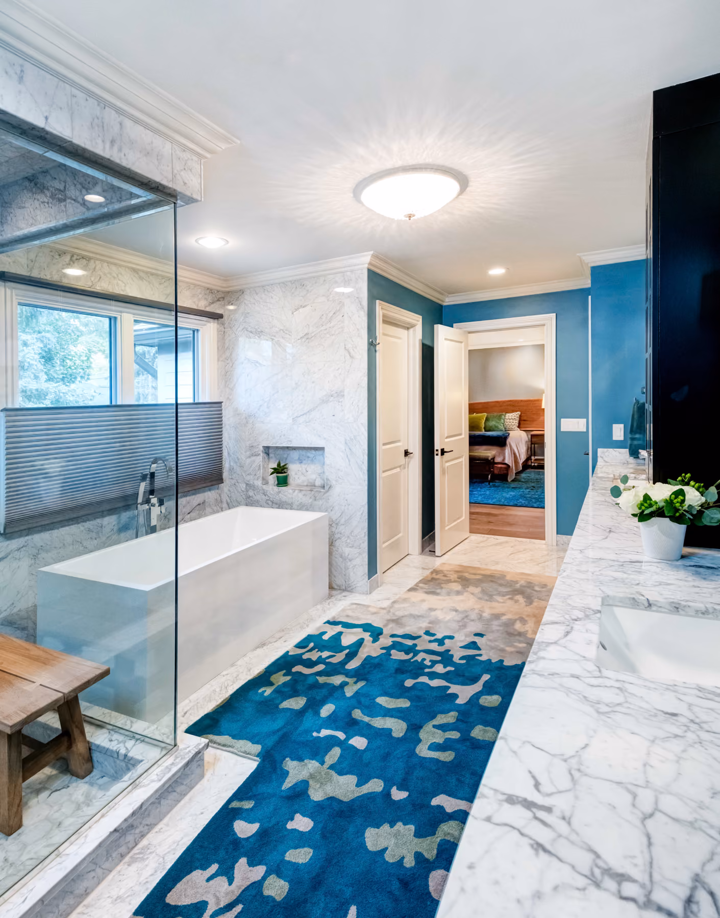 Primary bathroom with marble-clad walls, a freestanding soaking tub, a glass-enclosed shower, and a blue floral area rug