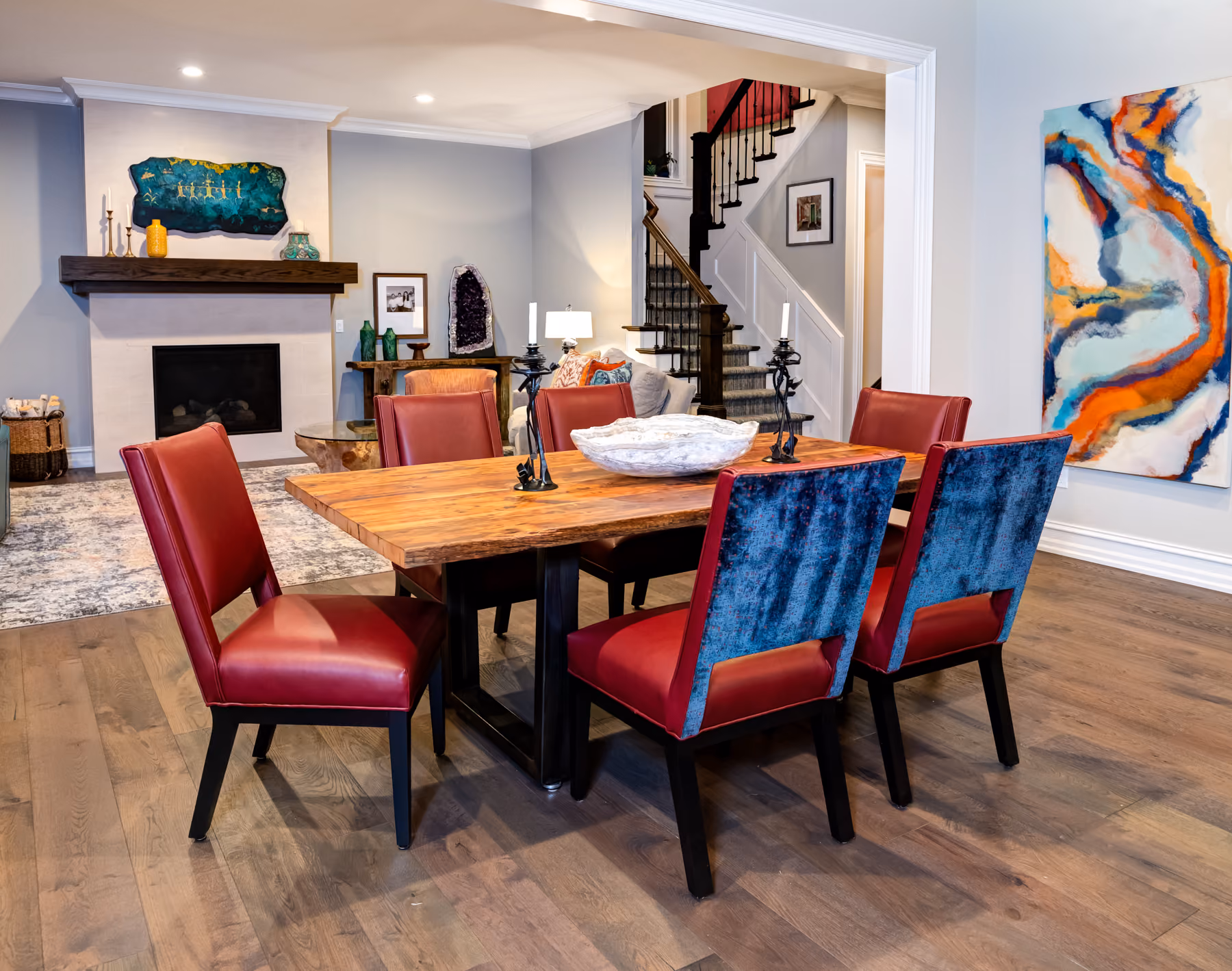 Dining room with a live-edge wood table, mixed red leather and blue velvet chairs, and a large abstract painting