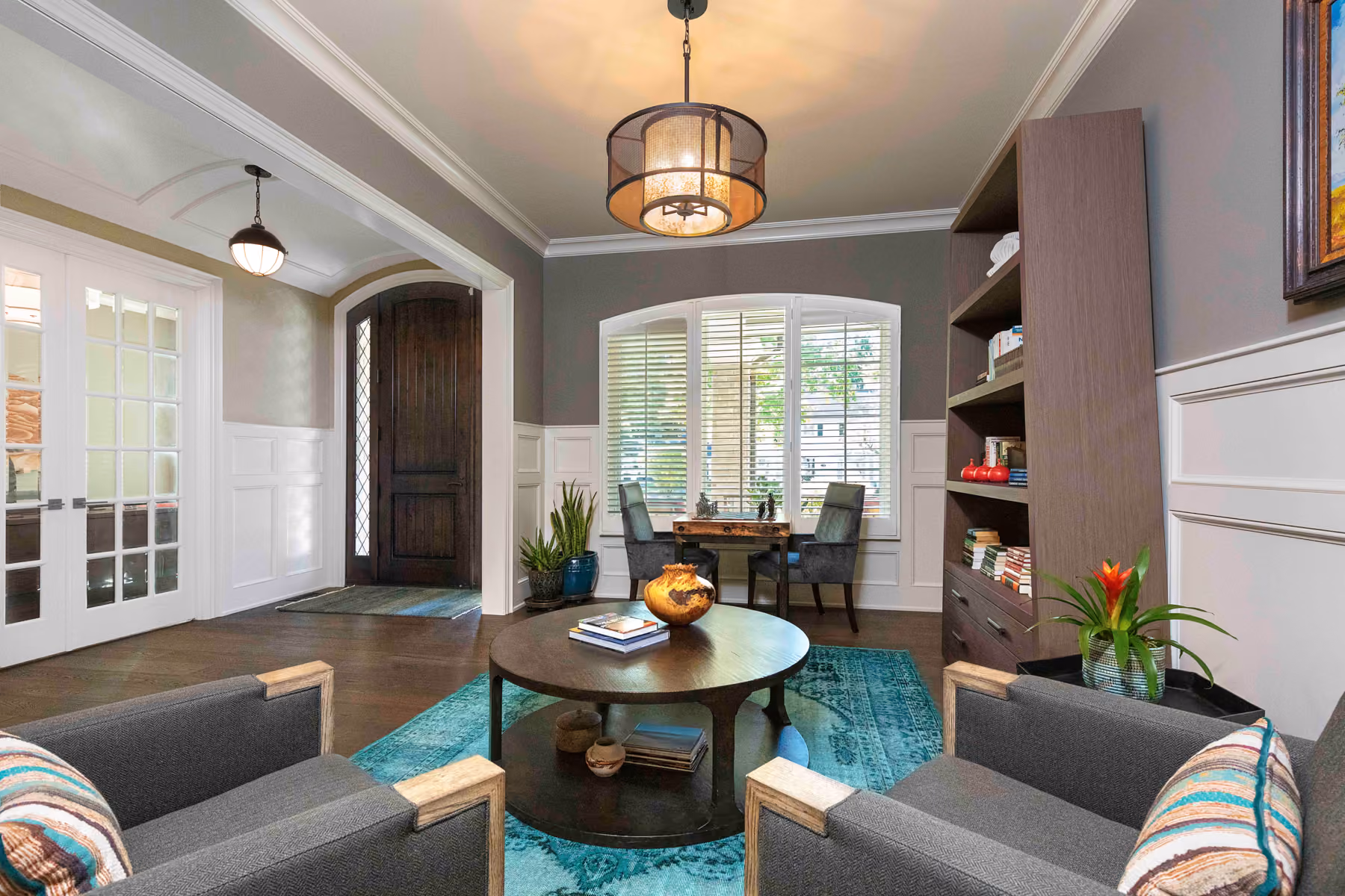 Sitting room off the entry with gray armchairs, a round wood coffee table, a teal patterned rug, and a wood-paneled front door