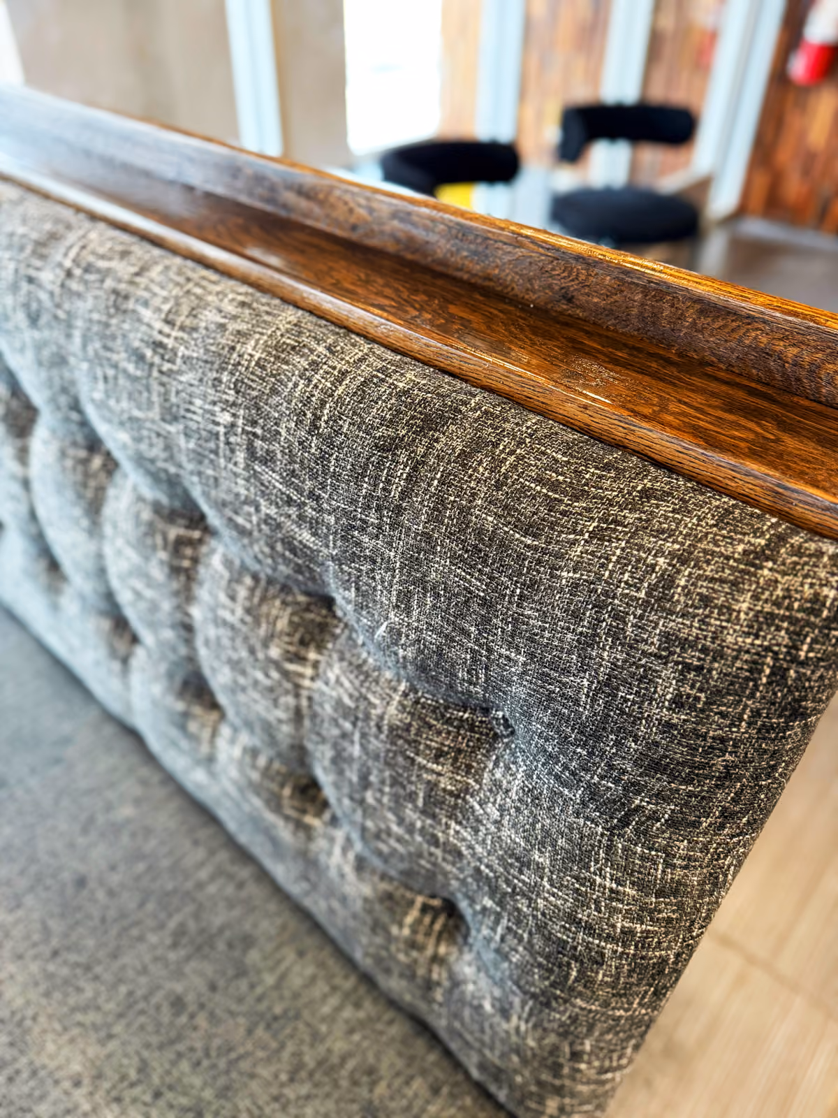 Detail of a tufted gray banquette seat back with a wood cap rail