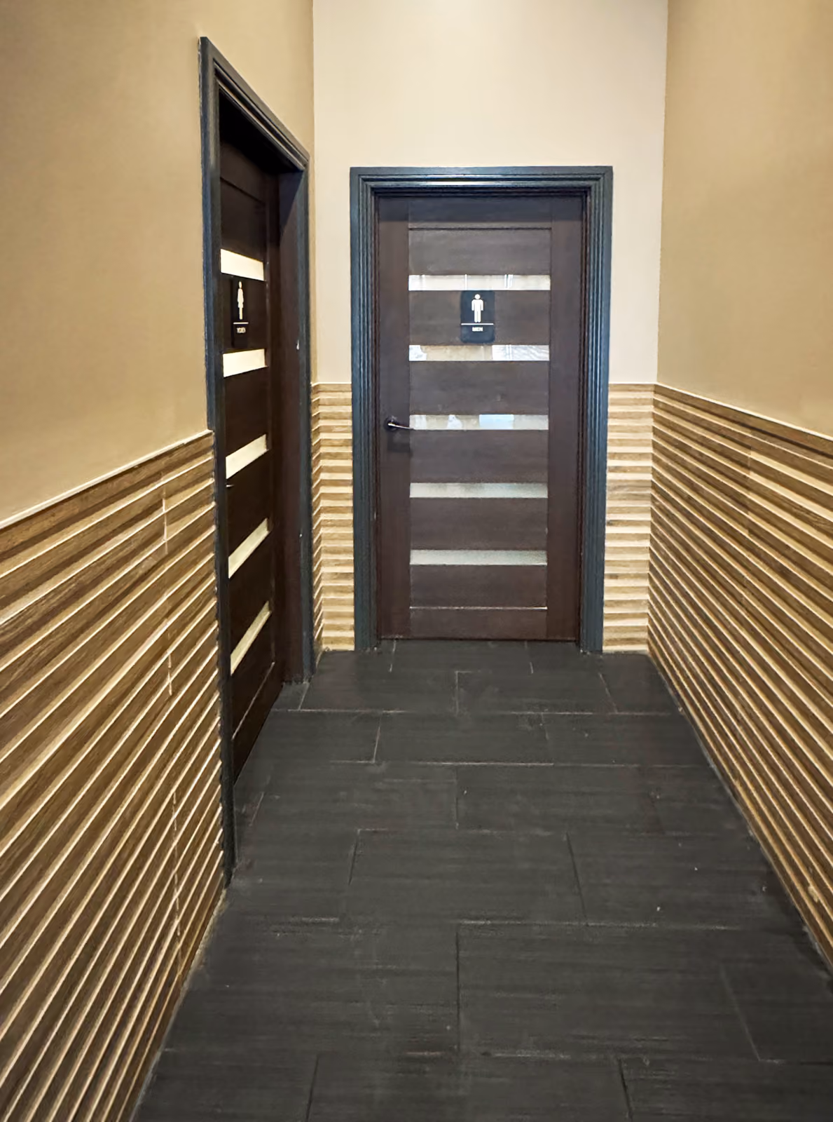 Hallway to the restrooms with striped wood-slat wainscoting and dark wood doors