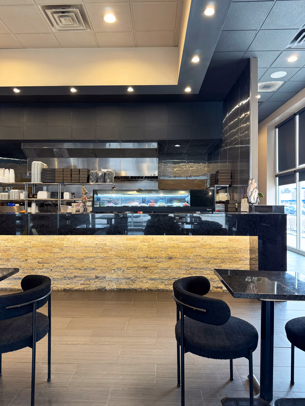 Open kitchen pass-through with black tile paneling, stainless steel equipment, and a glowing stone counter front