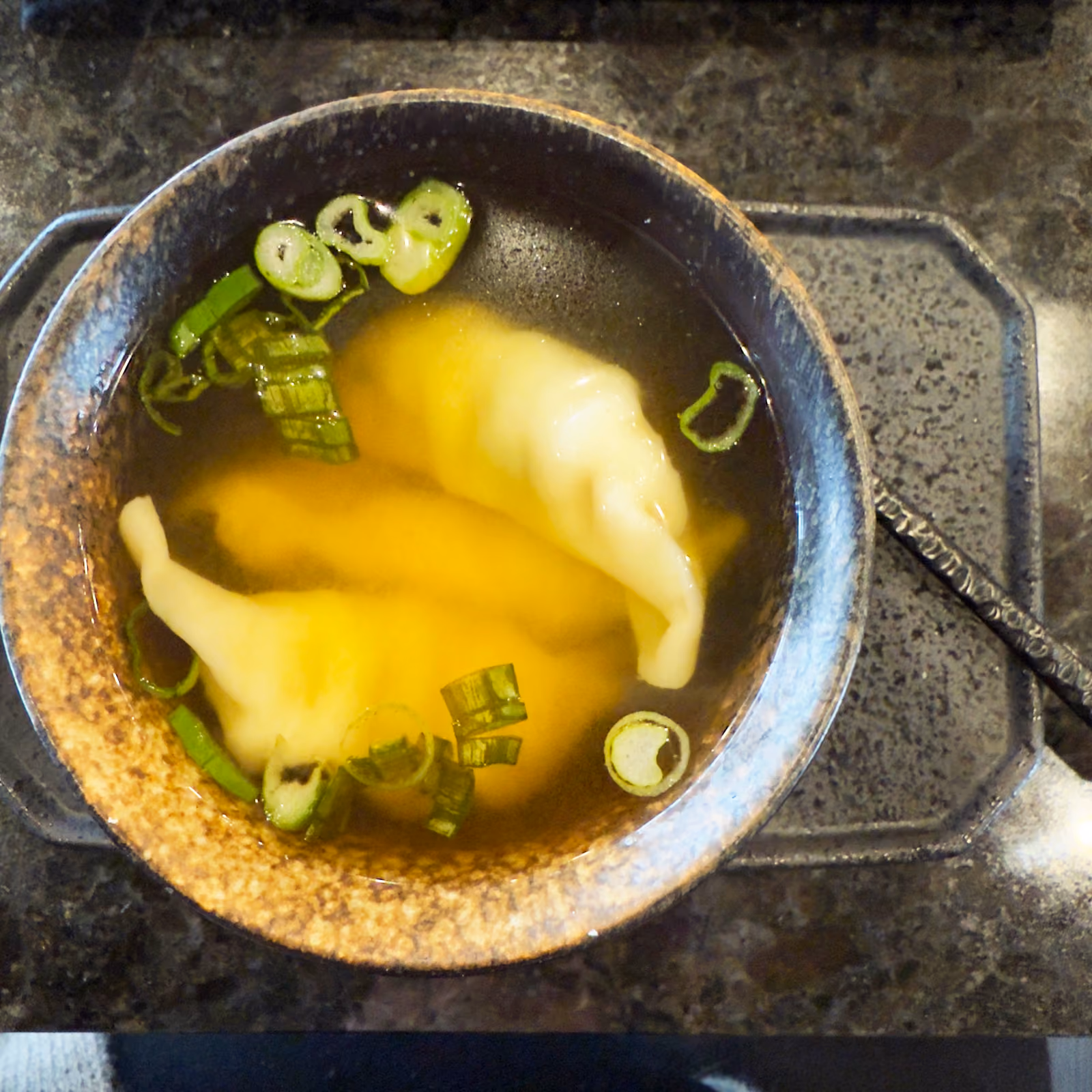 Bowl of wonton soup with dumplings and scallions on the granite counter