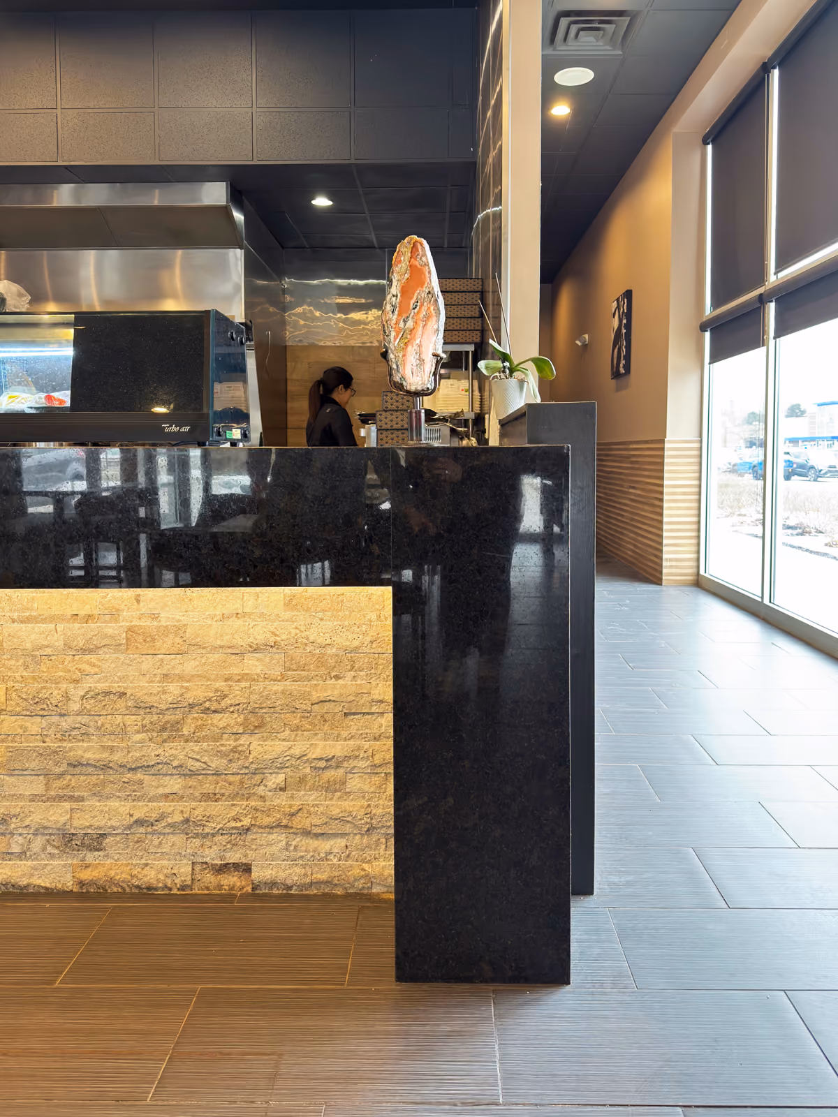 Counter-end detail with a black granite waterfall edge, glowing stone tile front, and the open kitchen beyond