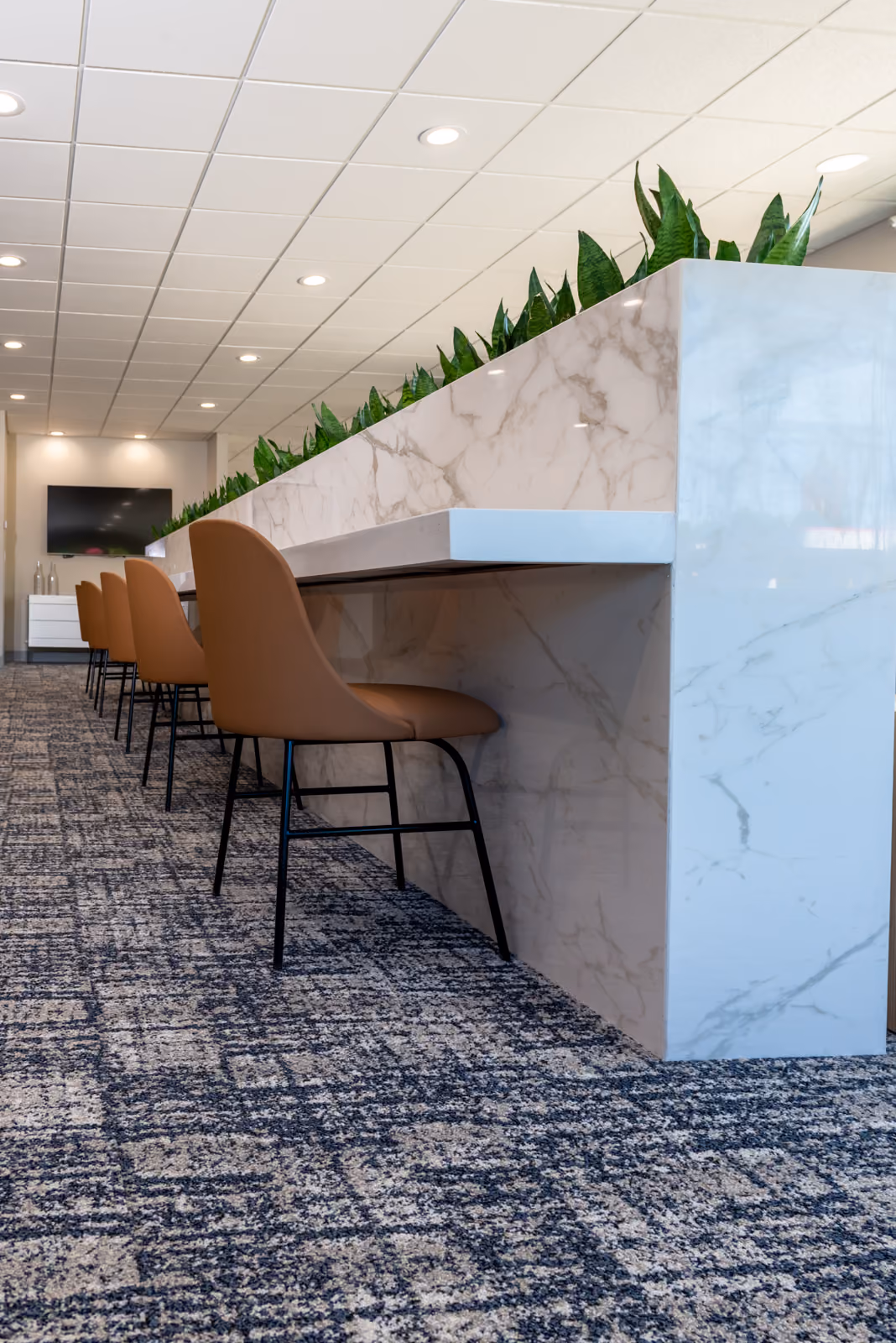 Workstation counter with a marble waterfall base, cognac leather task chairs, and integrated planters