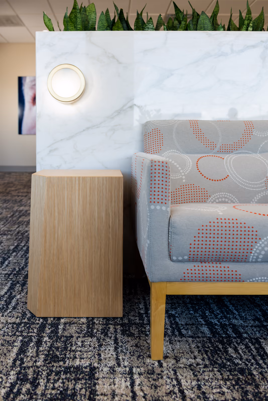 Detail of a dot-pattern lounge chair and wood side table beside the marble planter wall