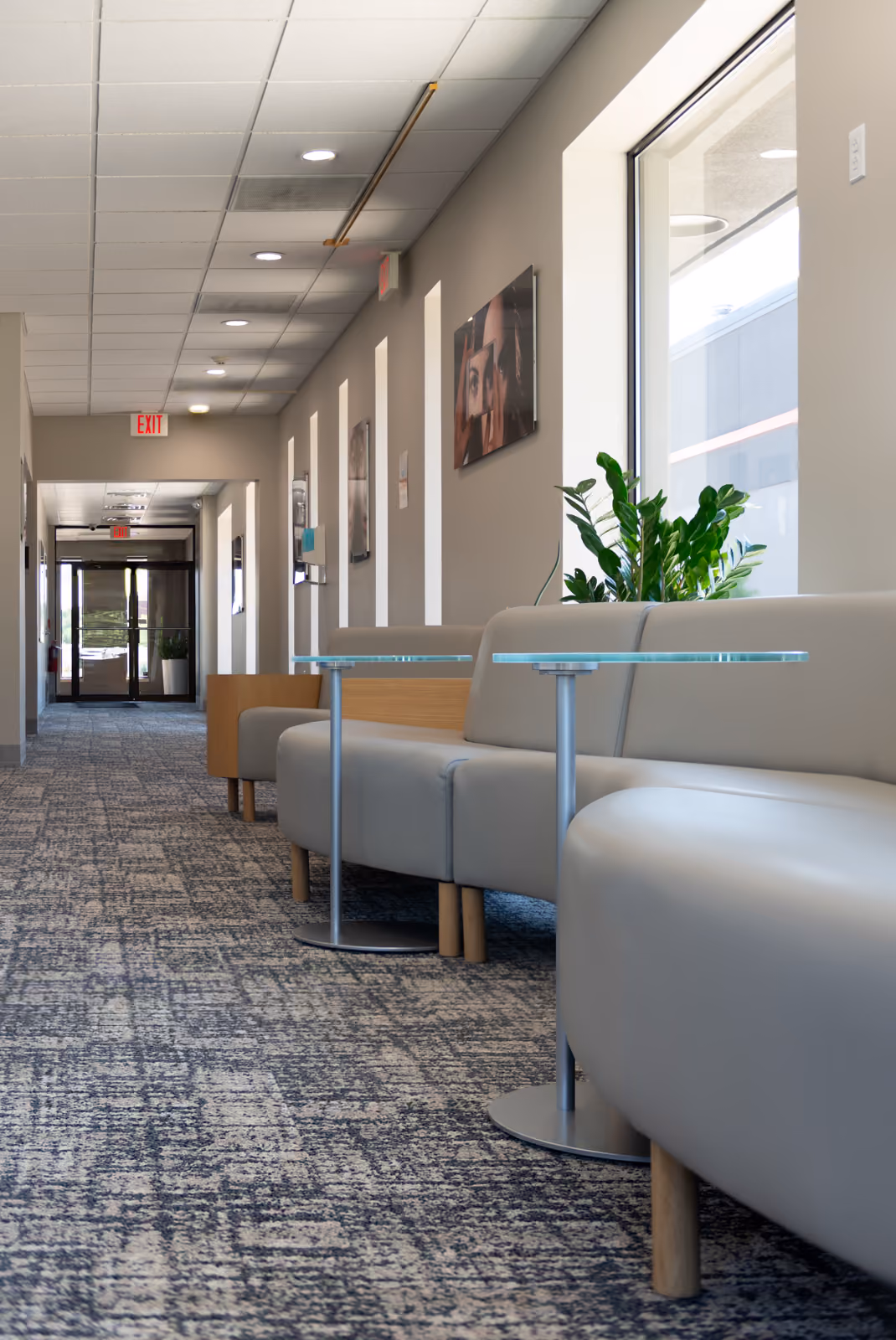 Hallway with rounded gray upholstered bench seating, glass-top side tables, and framed art