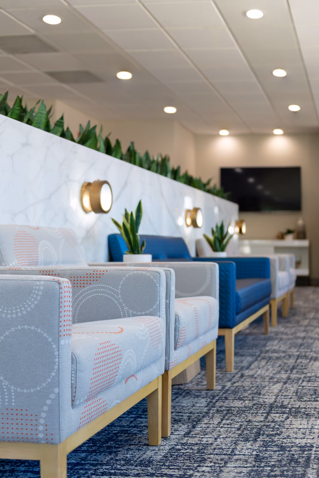 Waiting room chairs in dot-print and navy upholstery along a marble planter wall with brass sconces