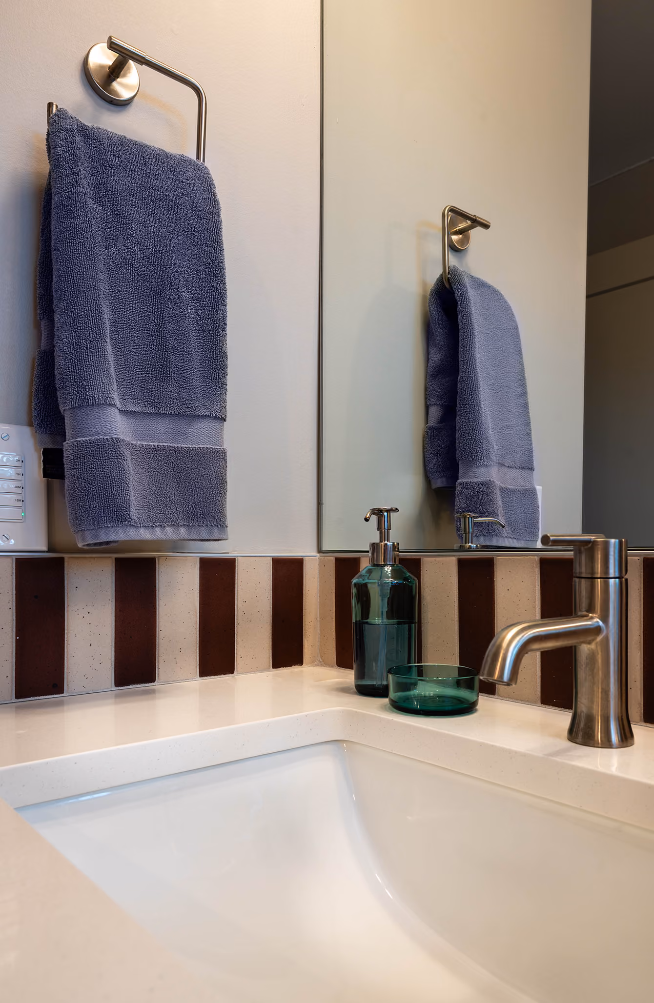 Bathroom sink detail with hand towel, soap dispenser, and striped tile backsplash