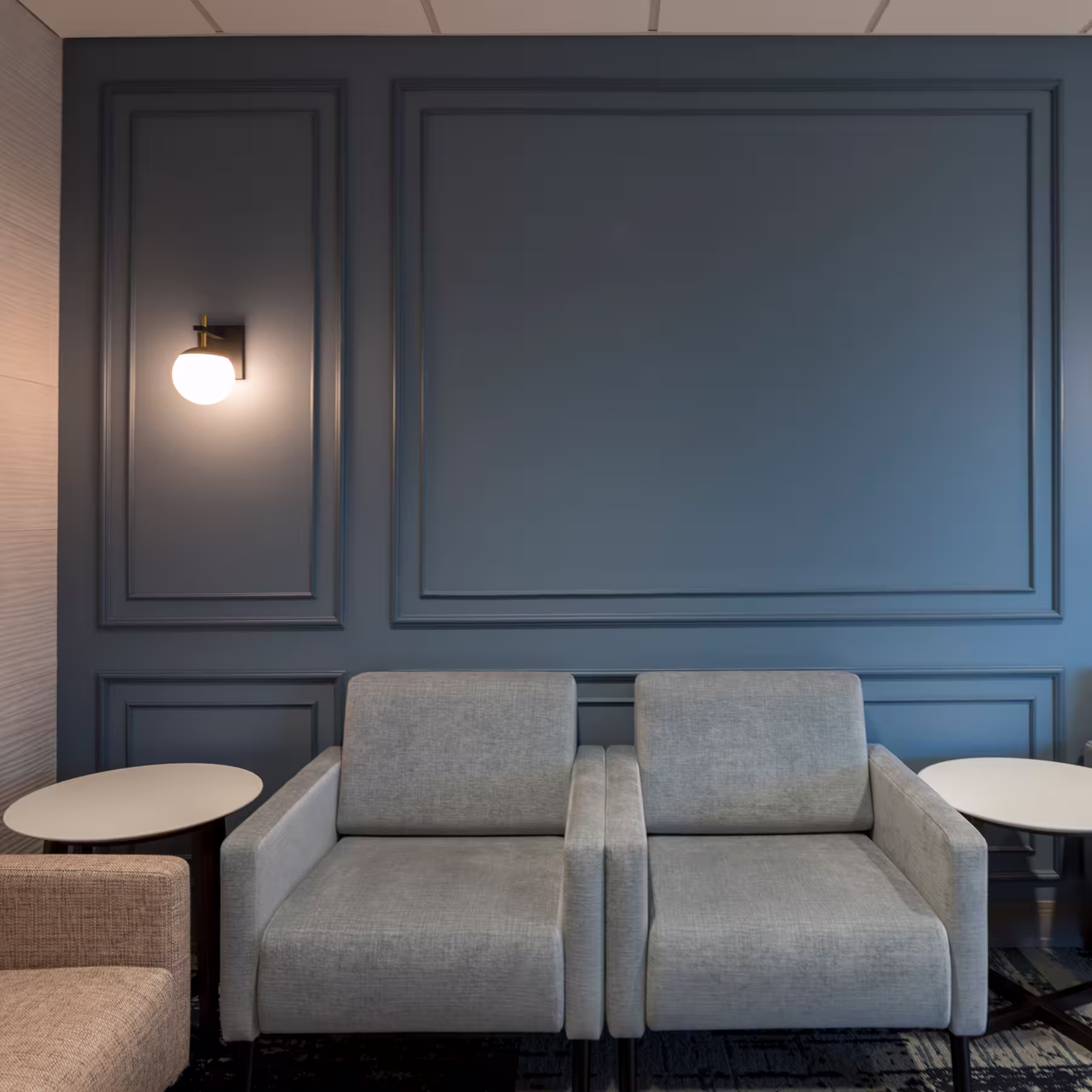 Waiting room seating area with a navy blue paneled accent wall, wall sconces, and gray upholstered lounge chairs