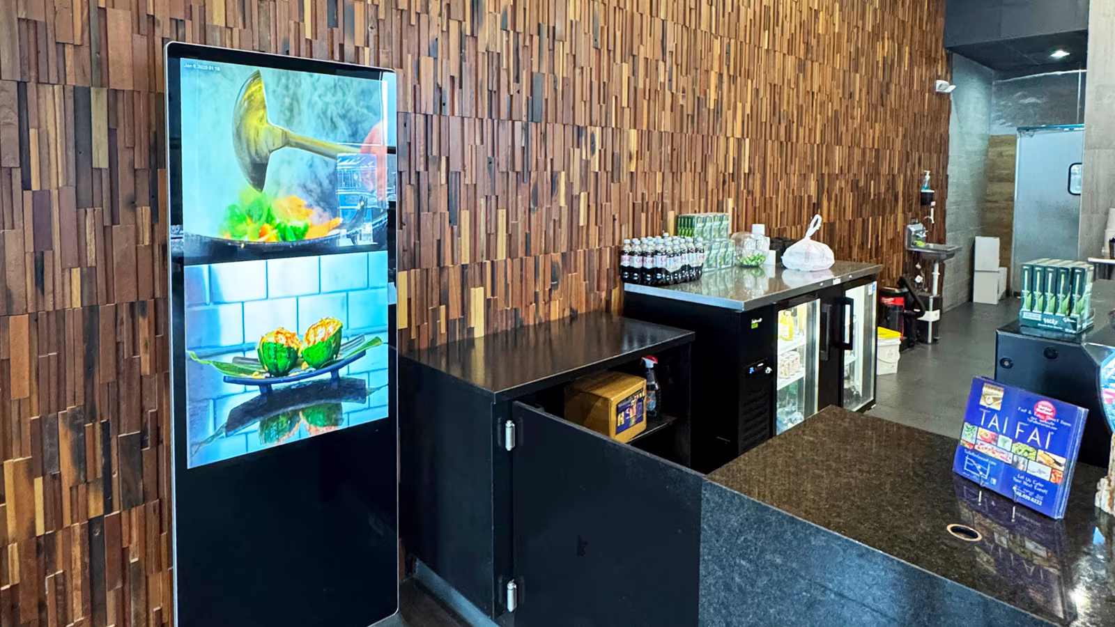 Restaurant counter with a dramatic 3D wood block accent wall, a digital menu display, and a dark granite bar