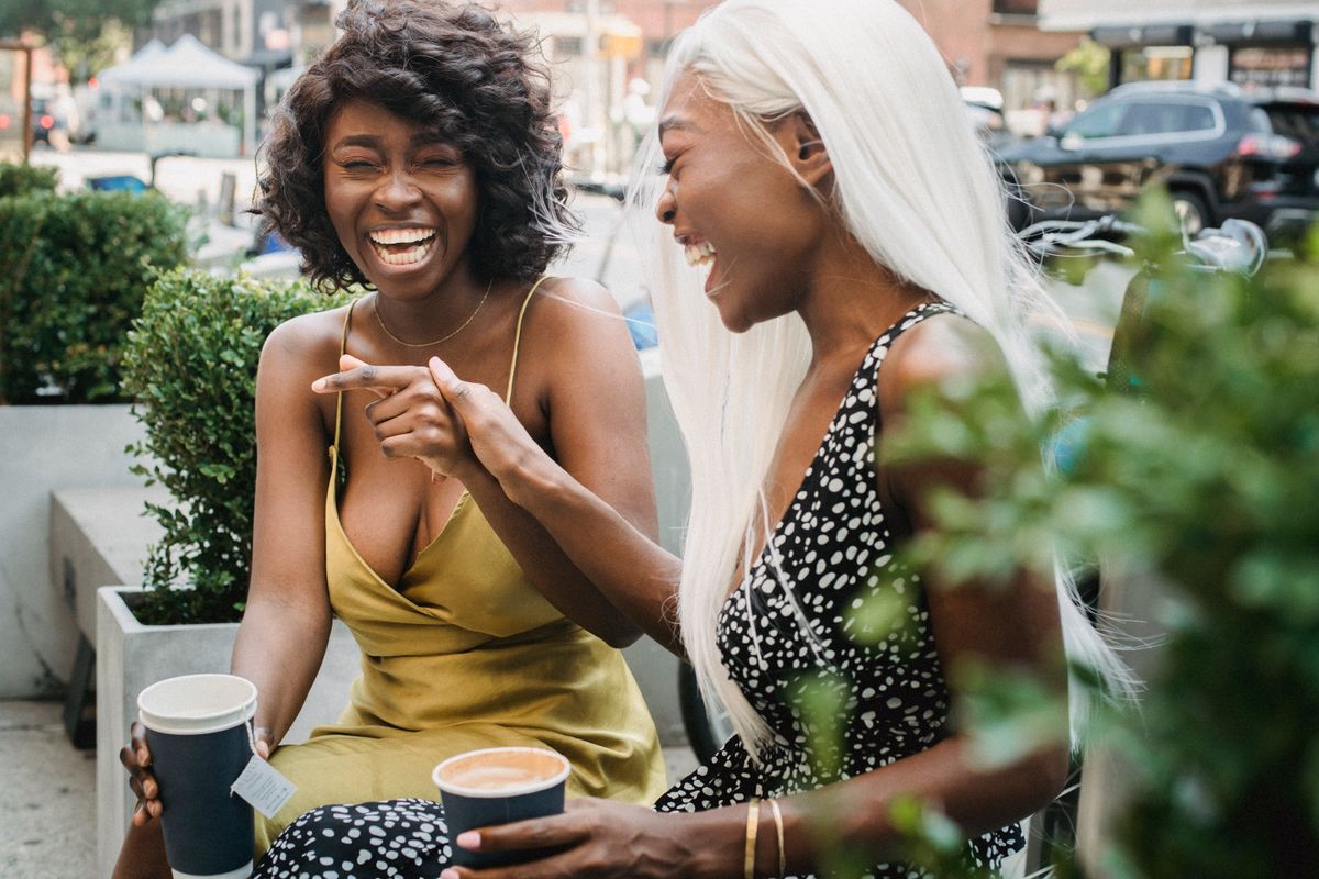 Two friends laughing over hot drinks outdoors