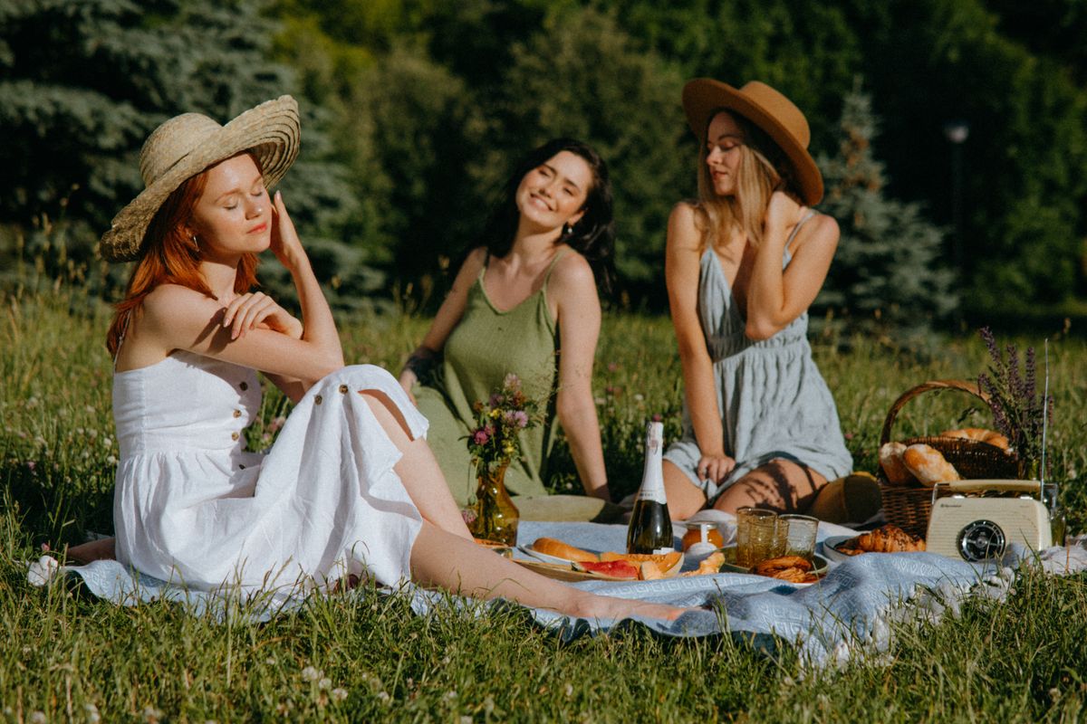 Three friends sharing food and laughter at a sunny picnic