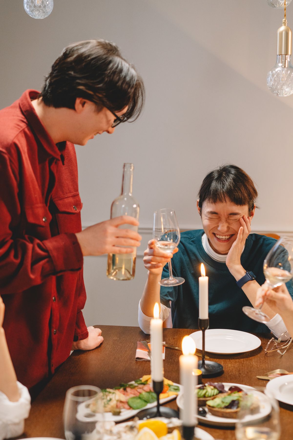 Two friends laughing over dinner, wine and candles