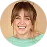 Smiling woman with light brown hair and bangs wearing a green top against a white background.