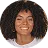 Smiling woman with curly hair in a brown top against a plain background.